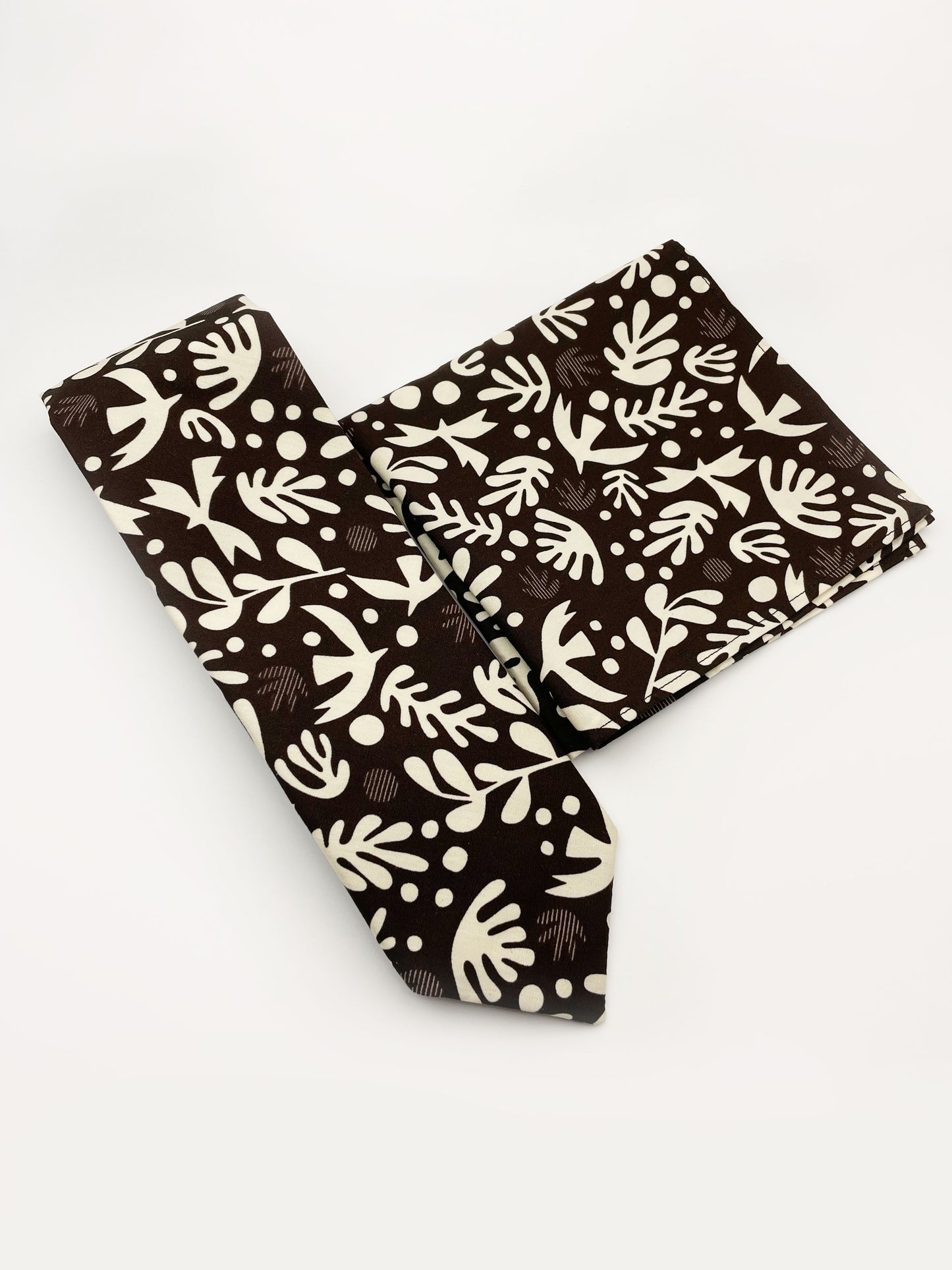 A cotton necktie with cream-colored birds and abstract shapes shown with a matching pocket square.