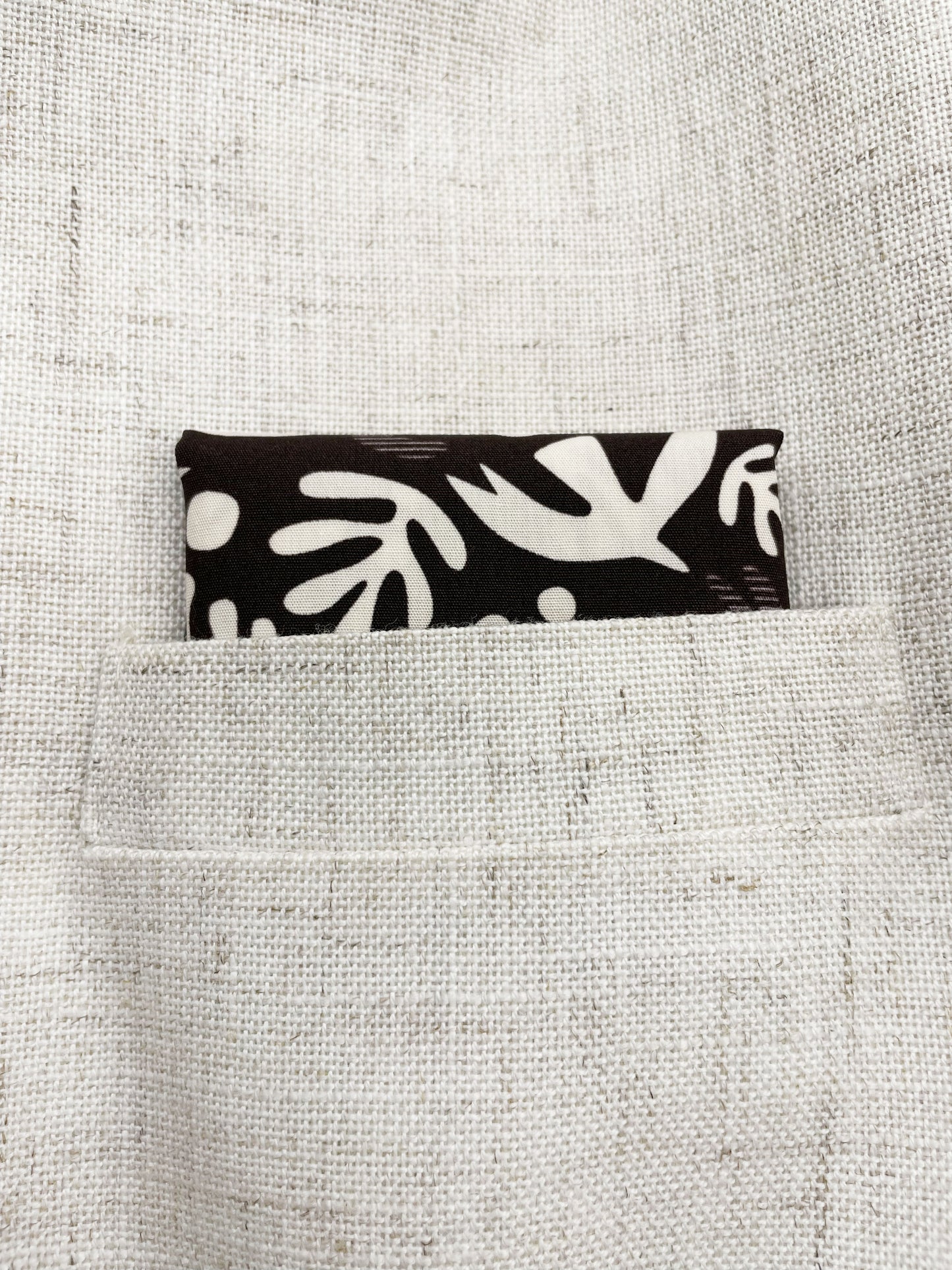A cotton handmade pocket square with cream-colored birds and abstract shapes shown in a suit jacket pocket.