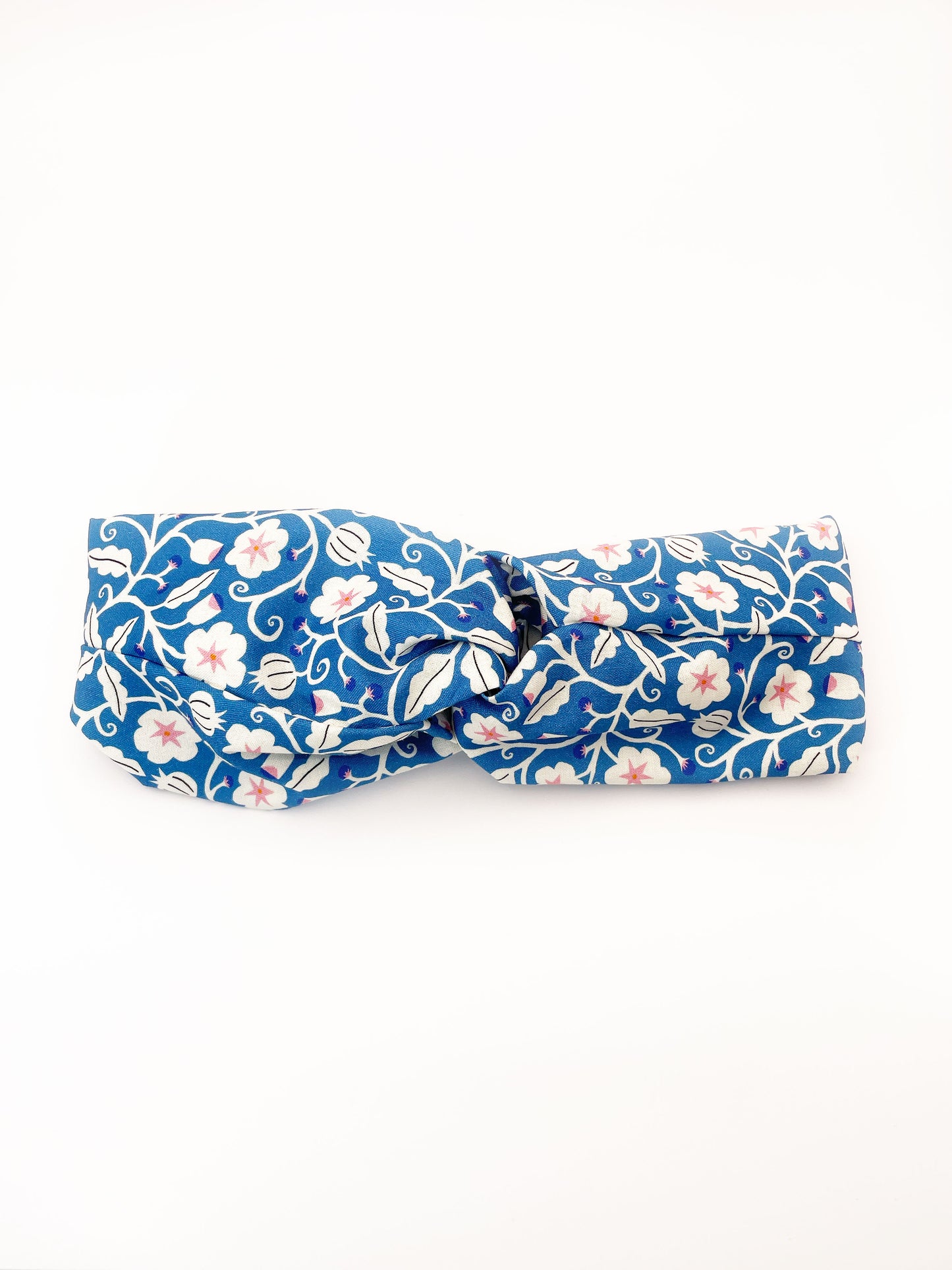 A blue twist headband with white flowers that have pink centers.
