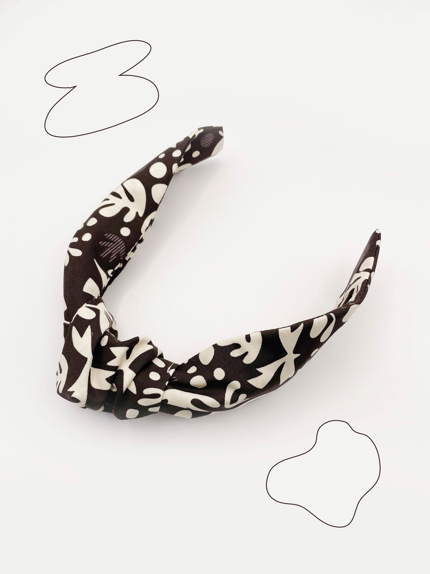 A dark charcoal gray knotted headband with cream-colored birds and abstract shapes. Each headband is crafted with cotton fabric attached to a durable hair band for a secure and comfortable fit.