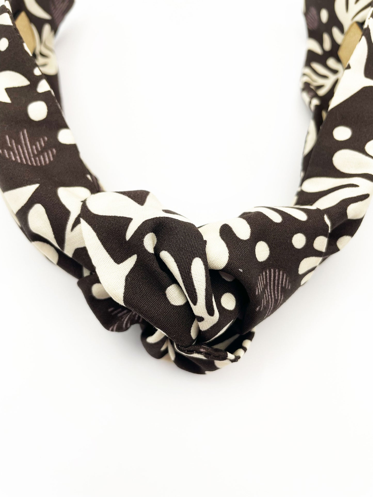 A dark charcoal gray knotted headband with cream-colored birds and abstract shapes. Each headband is crafted with cotton fabric attached to a durable hair band for a secure and comfortable fit.