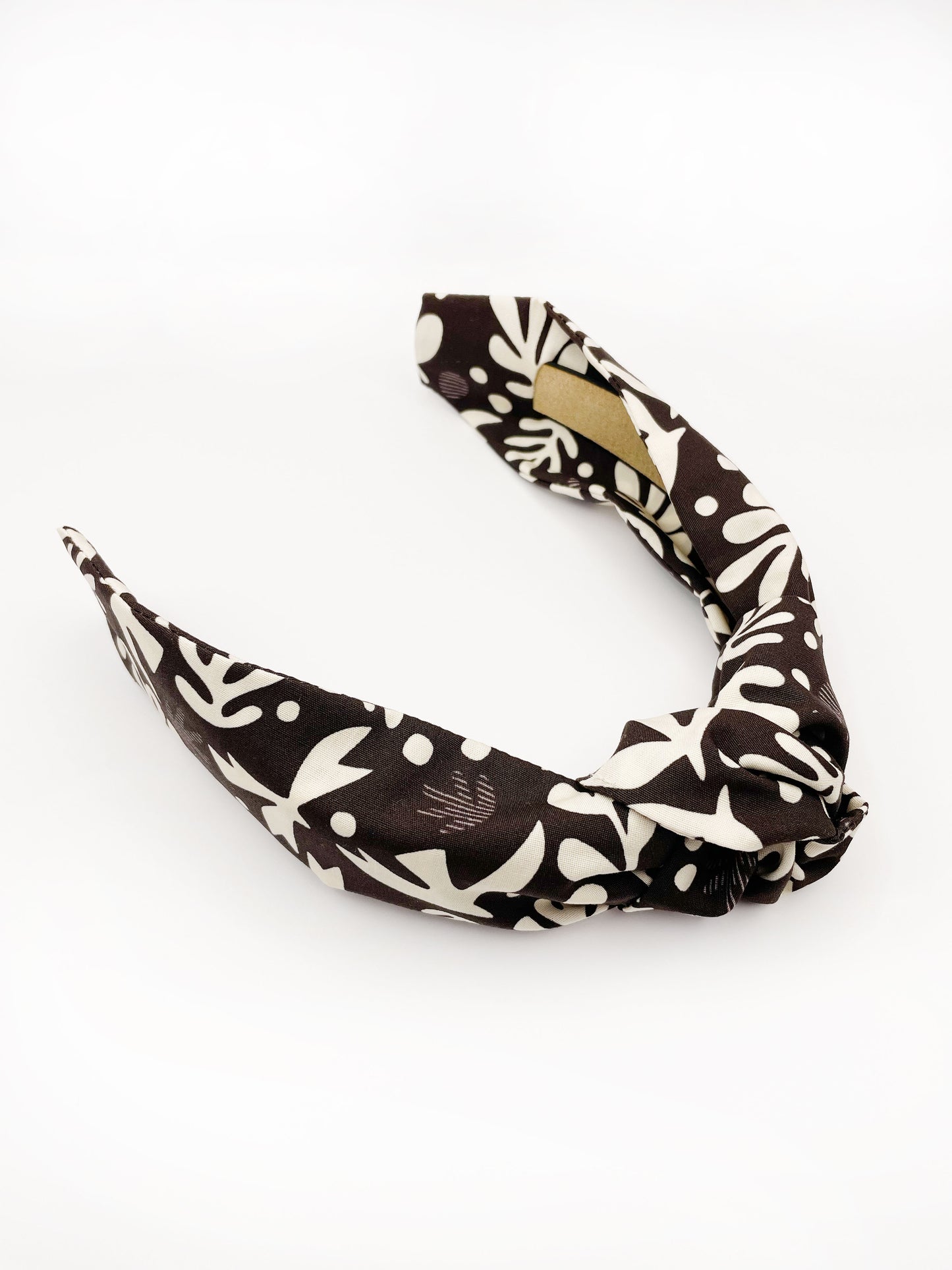 A dark charcoal gray knotted headband with cream-colored birds and abstract shapes. Each headband is crafted with cotton fabric attached to a durable hair band for a secure and comfortable fit.