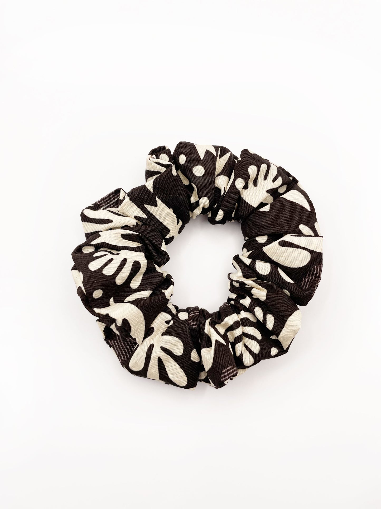 A dark charcoal gray scrunchie with cream-colored birds and abstract shapes. Made with 100% cotton fabric, these scrunchies are gentle on hair and comfortable to wear all day. 