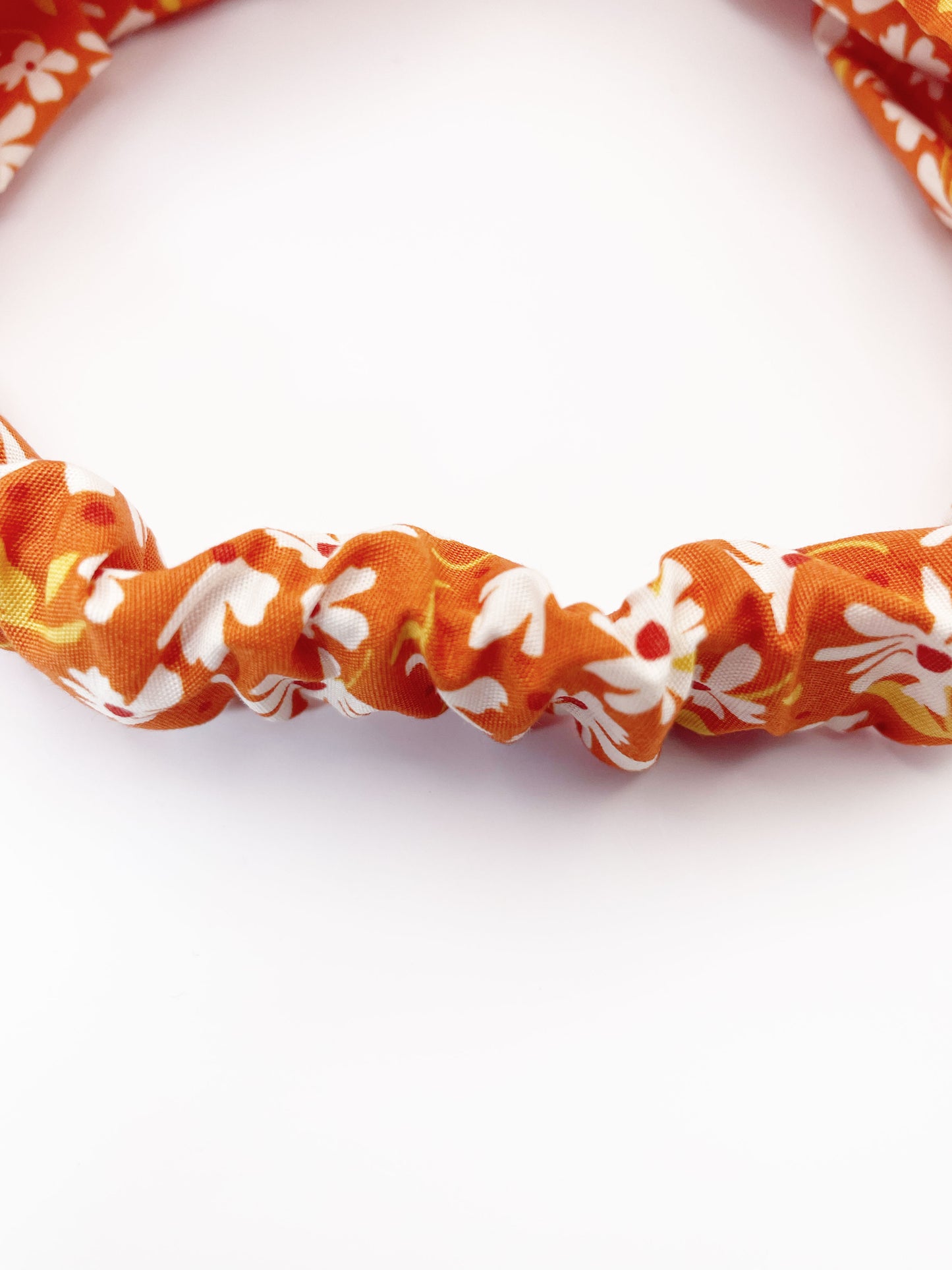 A handmade brown twist headband with off white flowers. The headband has an elastic band on the back.