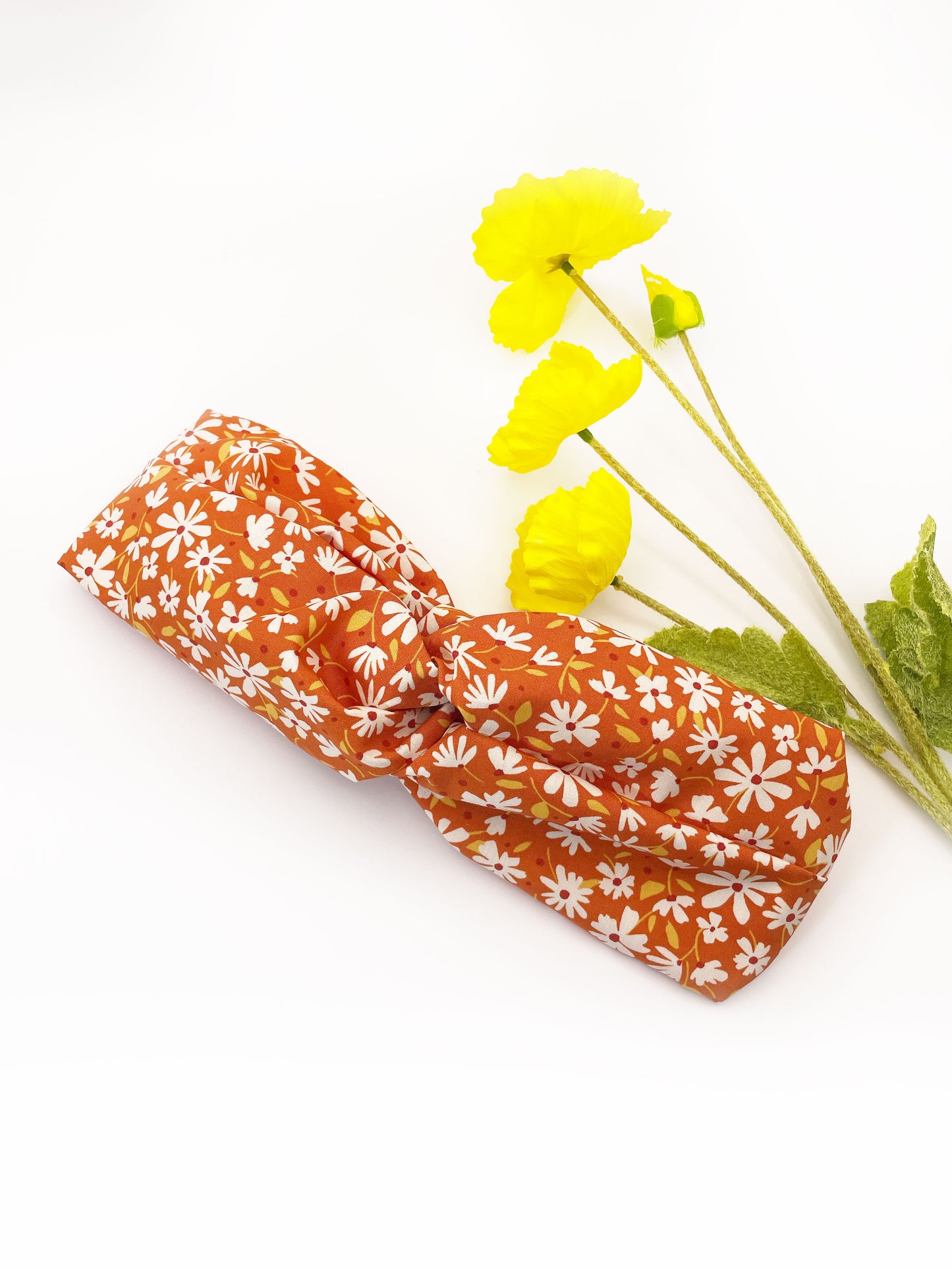 A handmade brown twist headband with off white flowers. The headband is next to yellow artificial flowers.