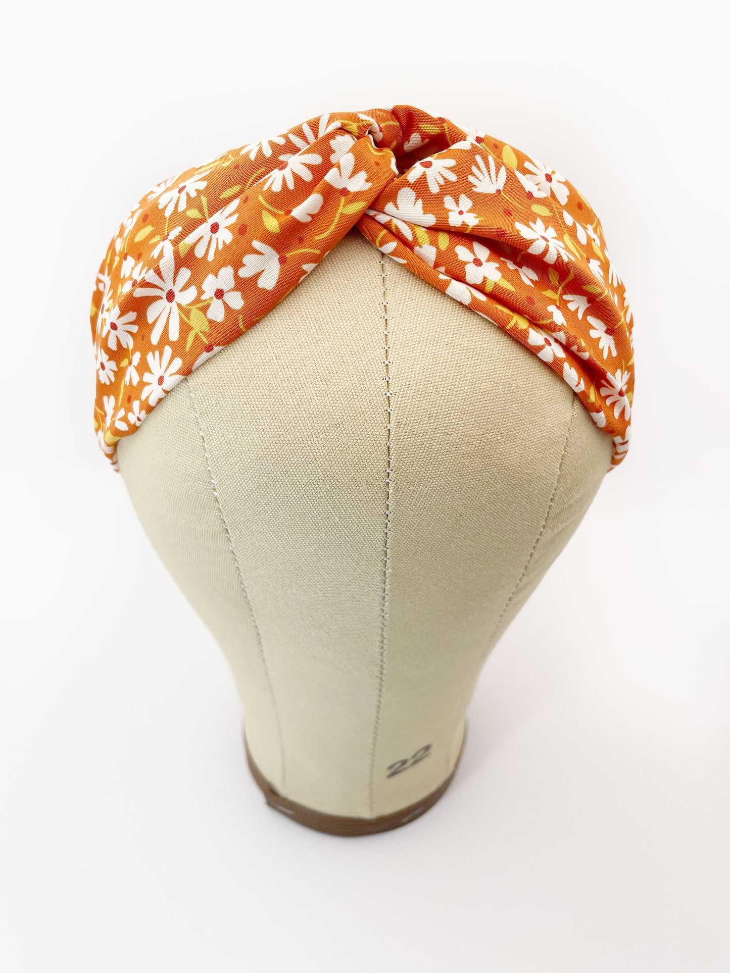 A handmade brown twist headband with off white flowers. The headband is modeled on a mannequin head.