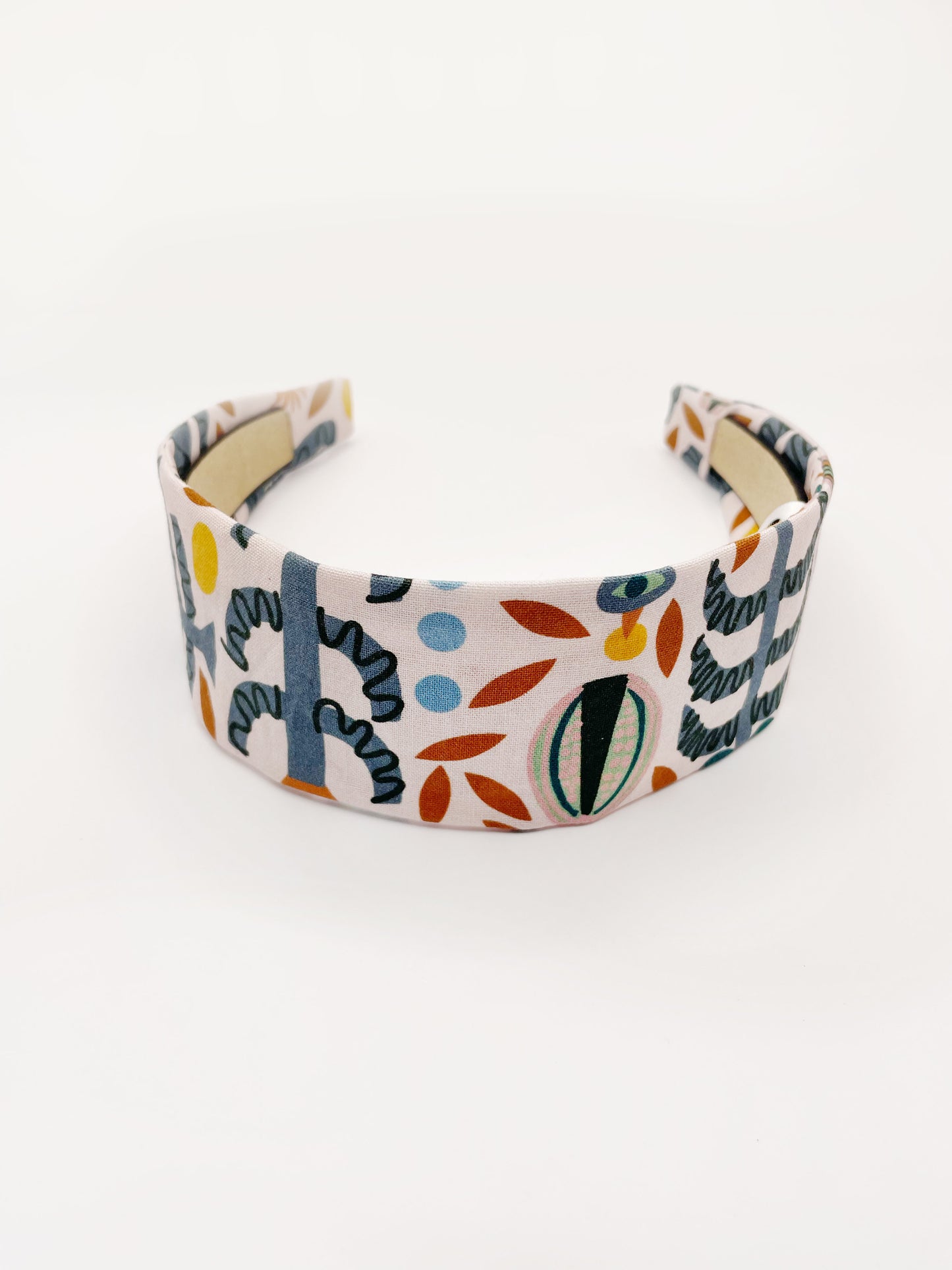 A fabric headband featuring a bold nature-inspired print of bugs, plants, suns, and rainbows.