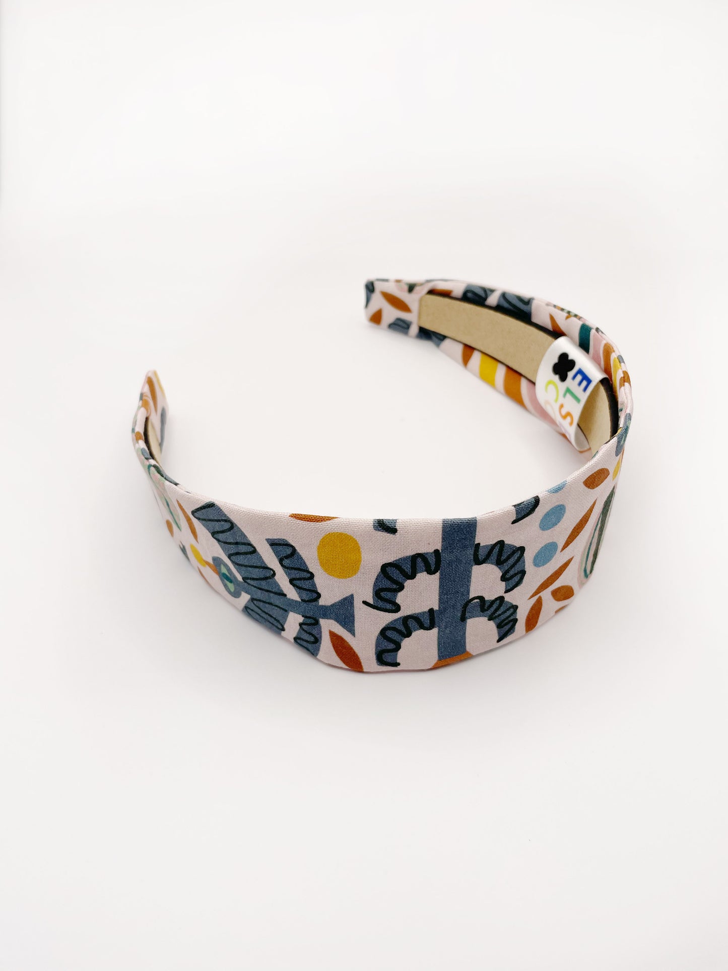 A fabric headband featuring a bold nature-inspired print of bugs, plants, suns, and rainbows.