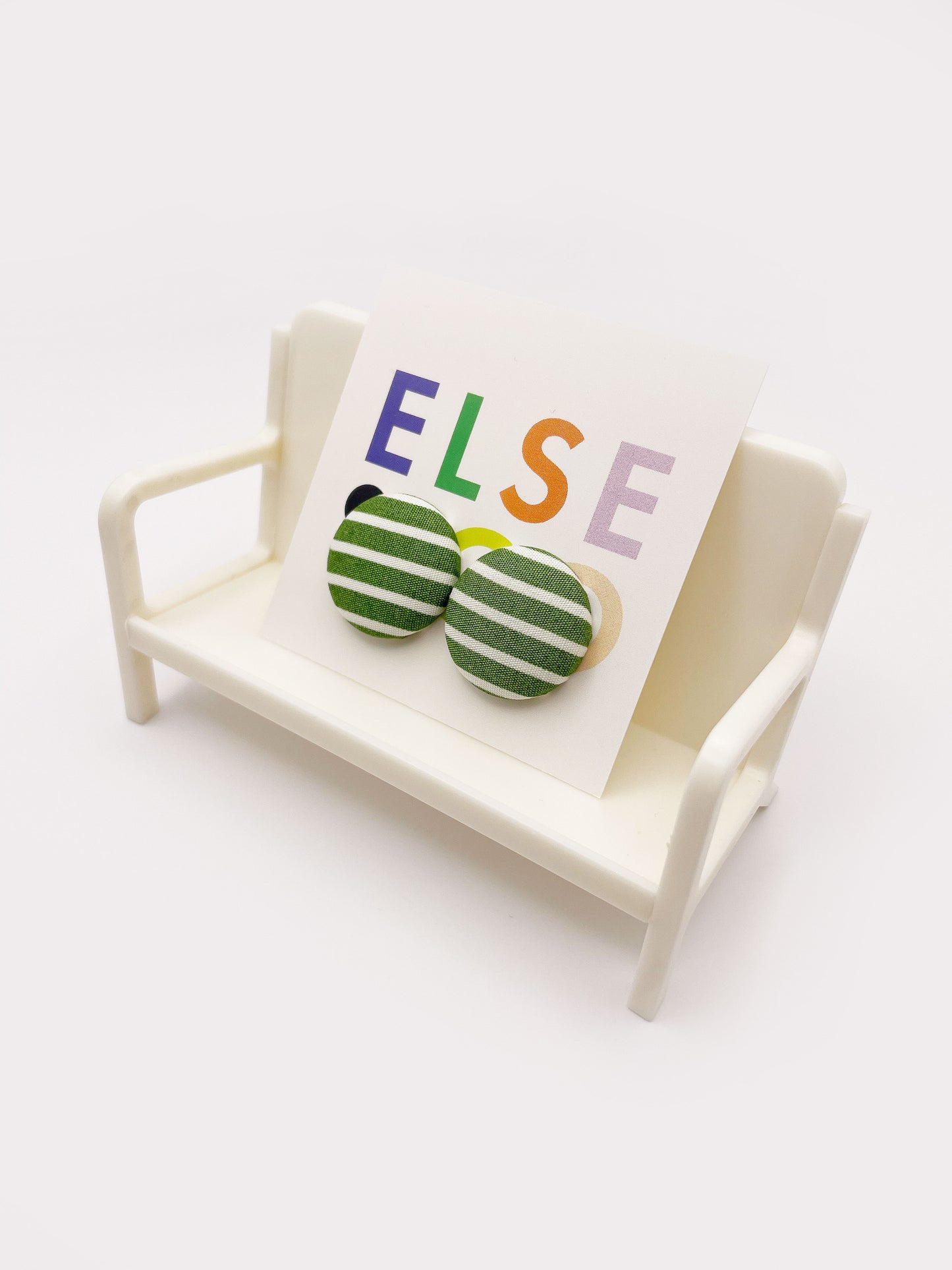 Handmade green striped fabric covered post earrings. The earrings are on a backing card that says "Else Co". The earrings are shown on a small white plastic chair.