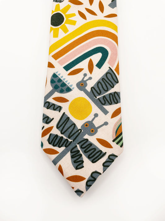A necktie featuring a bold nature-inspired print of bugs, plants, suns, and rainbows. The color palette includes muted mustard, gentle gray, and soft pastels.