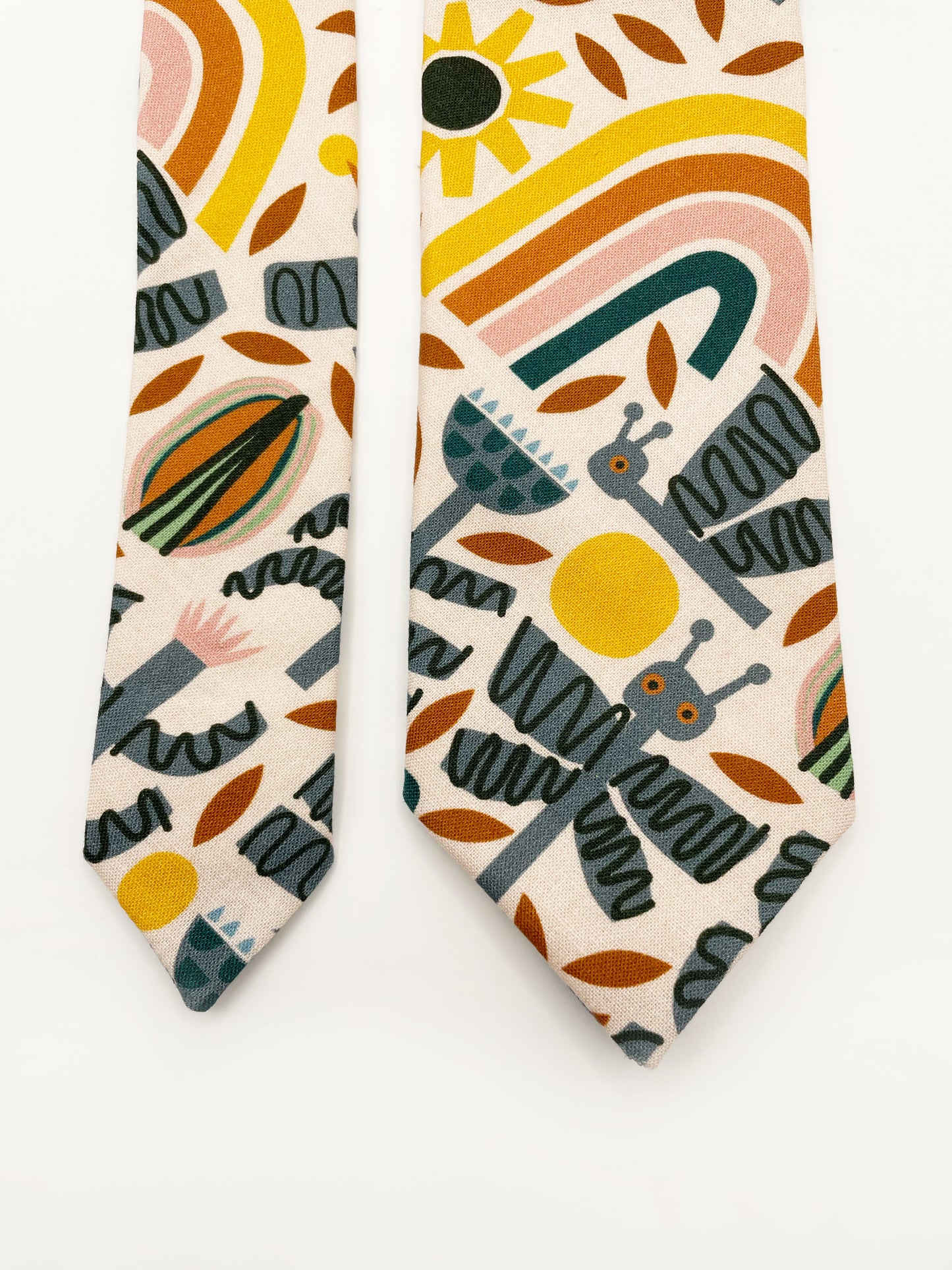 A necktie featuring a bold nature-inspired print of bugs, plants, suns, and rainbows. The color palette includes muted mustard, gentle gray, and soft pastels.