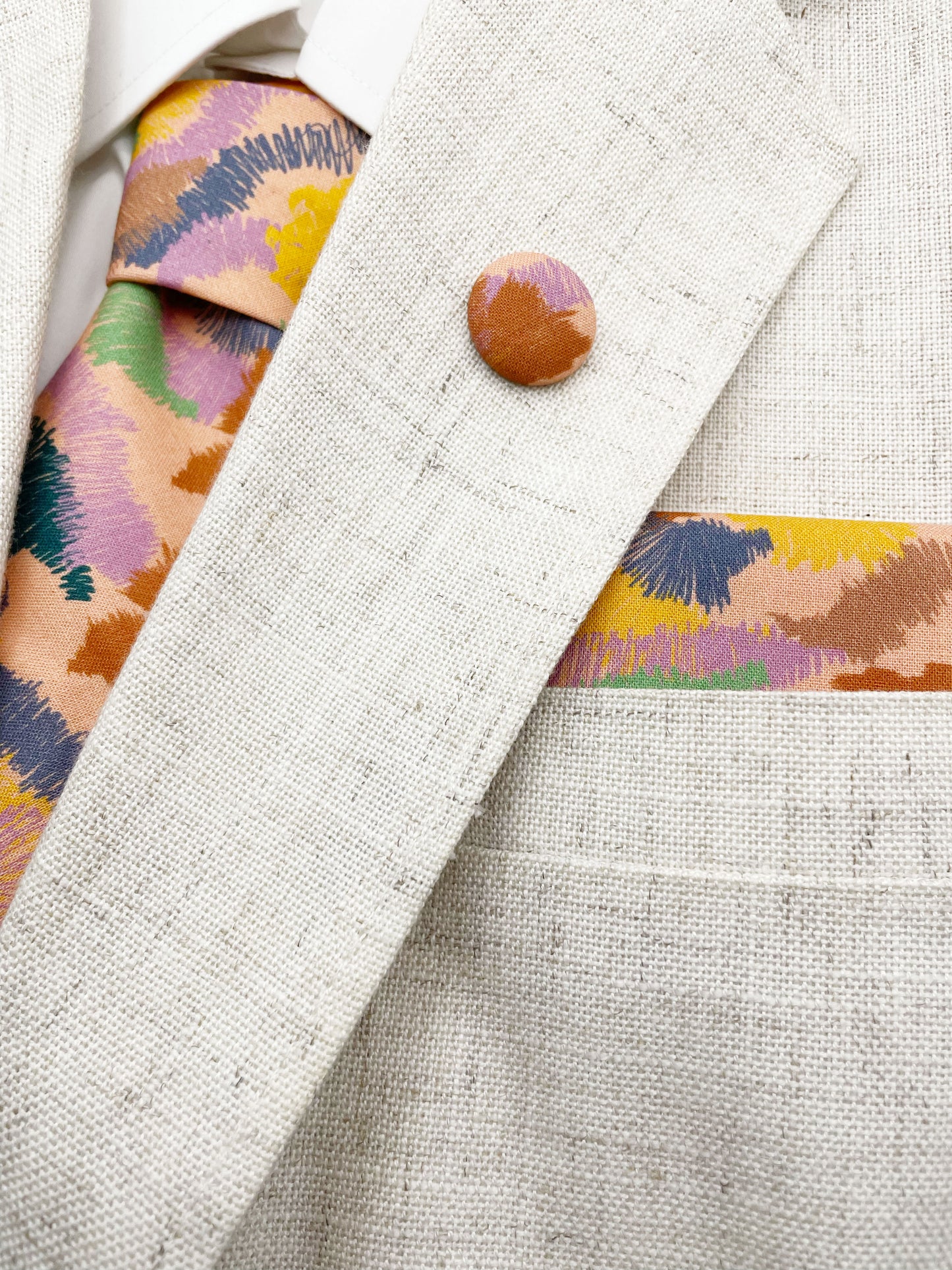 A necktie crafted from high-quality cotton with an abstract design inspired by the rolling hills and earthy tones of the desert. The necktie is shown with a matching pocket square and lapel pin.