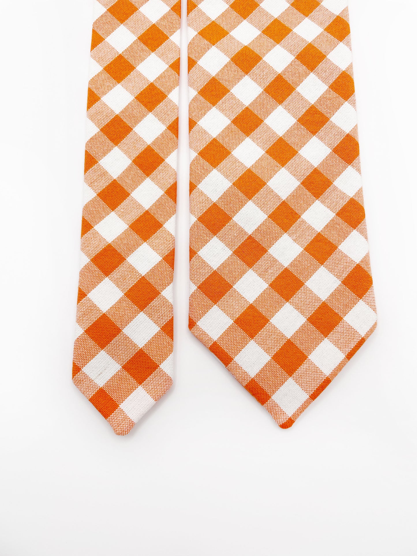 A cotton necktie with an orange and white gingham plaid print.
