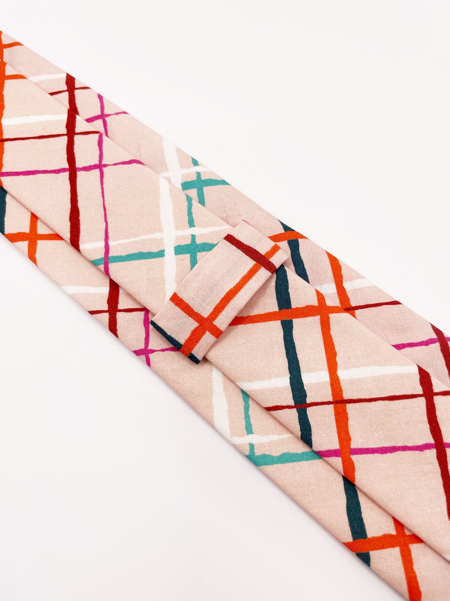 A handmade necktie featuring a colorful and modern plaid design with vibrant shades of pink, red, teal, and orange on a soft pastel background.