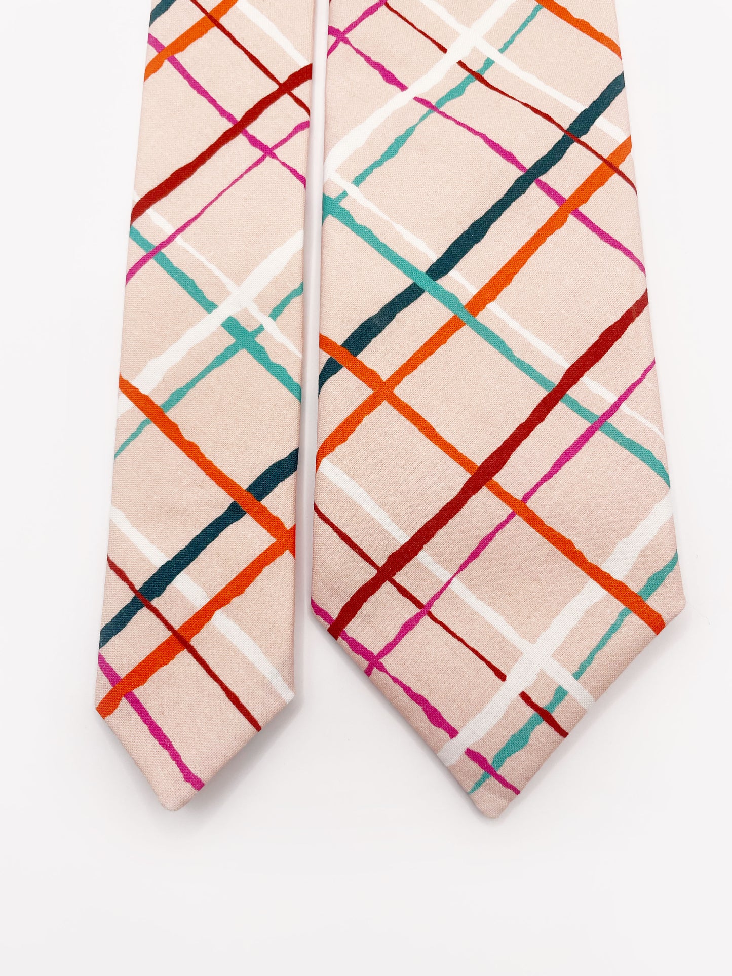 A handmade necktie featuring a colorful and modern plaid design with vibrant shades of pink, red, teal, and orange on a soft pastel background.