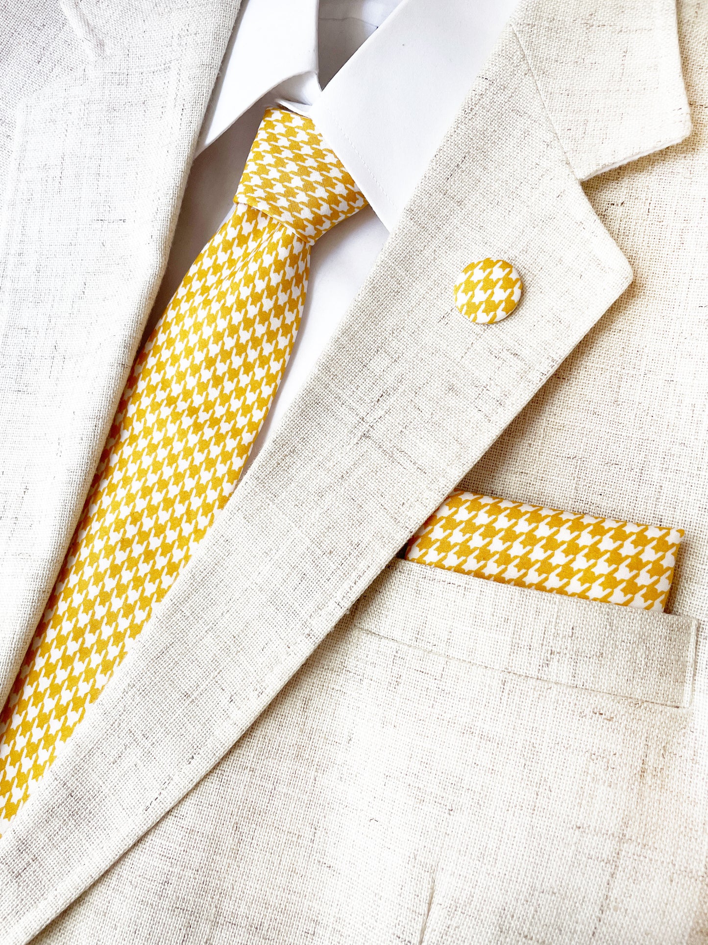 A handmade yellow houndstooth necktie with a matching pocket square and lapel pin.