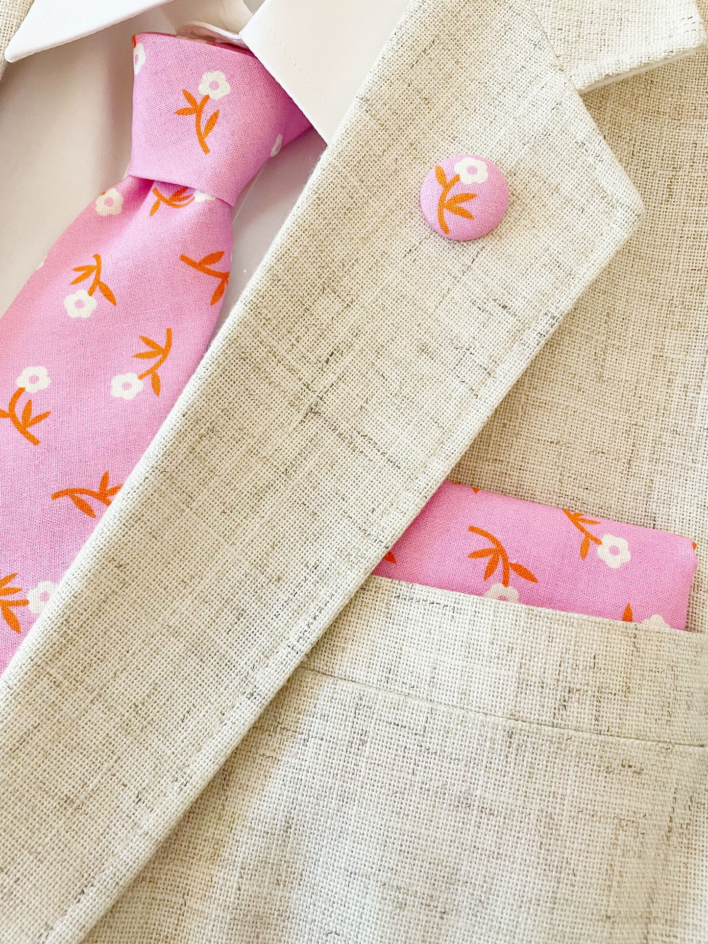 A cheerful pink pocket square with orange-stemmed flowers. The pocket square is modeled with a matching necktie and lapel pin. The necktie is sold separately.