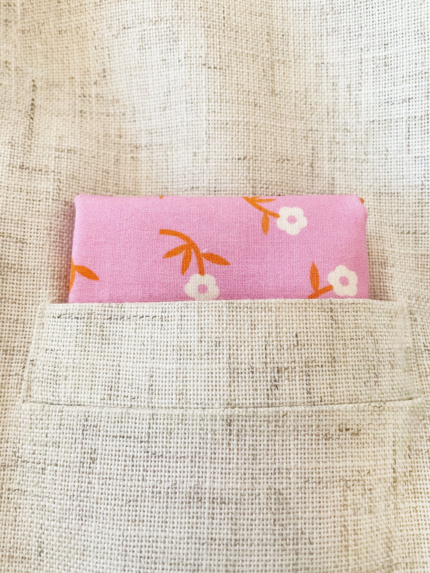 A cheerful pink pocket square with orange-stemmed flowers. The square is folded inside the pocket of a light tan jacket.