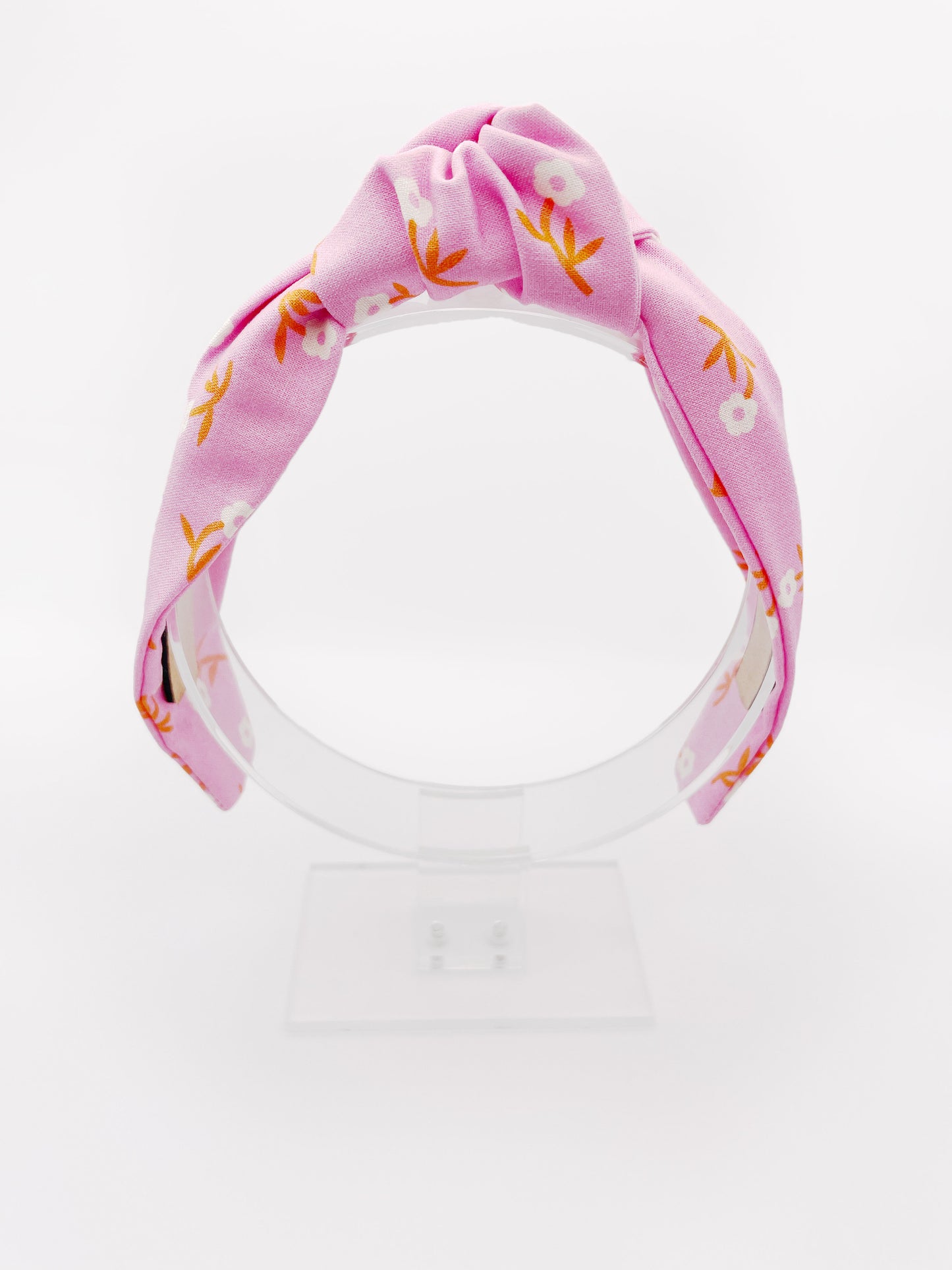 A cheerful pink knotted headband with orange-stemmed flowers.