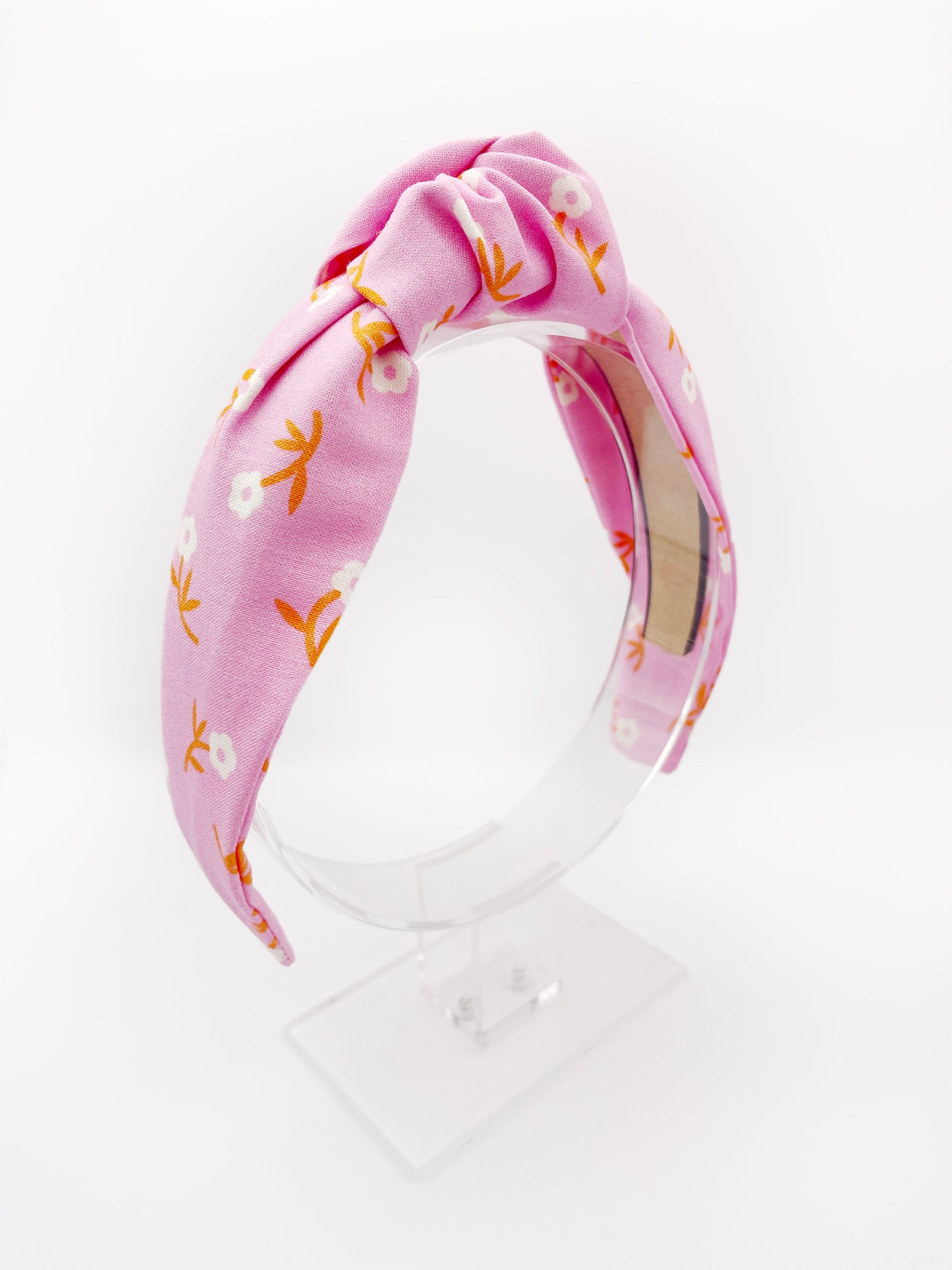 A cheerful pink knotted headband with orange-stemmed flowers.