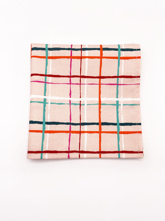 A handmade pocket square featuring a colorful and modern plaid design with vibrant shades of pink, red, teal, and orange on a soft pastel background.