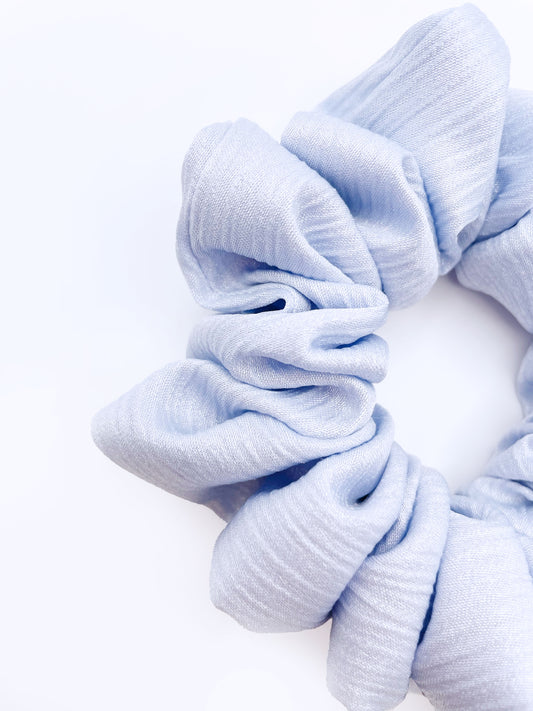 A scrunchie made with a light sky blue crinkle satin fabric.