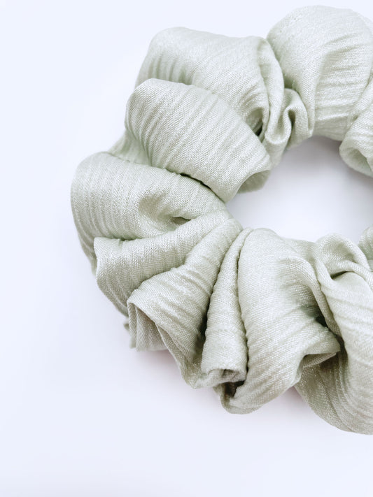A scrunchie made with a sage green crinkle satin fabric.