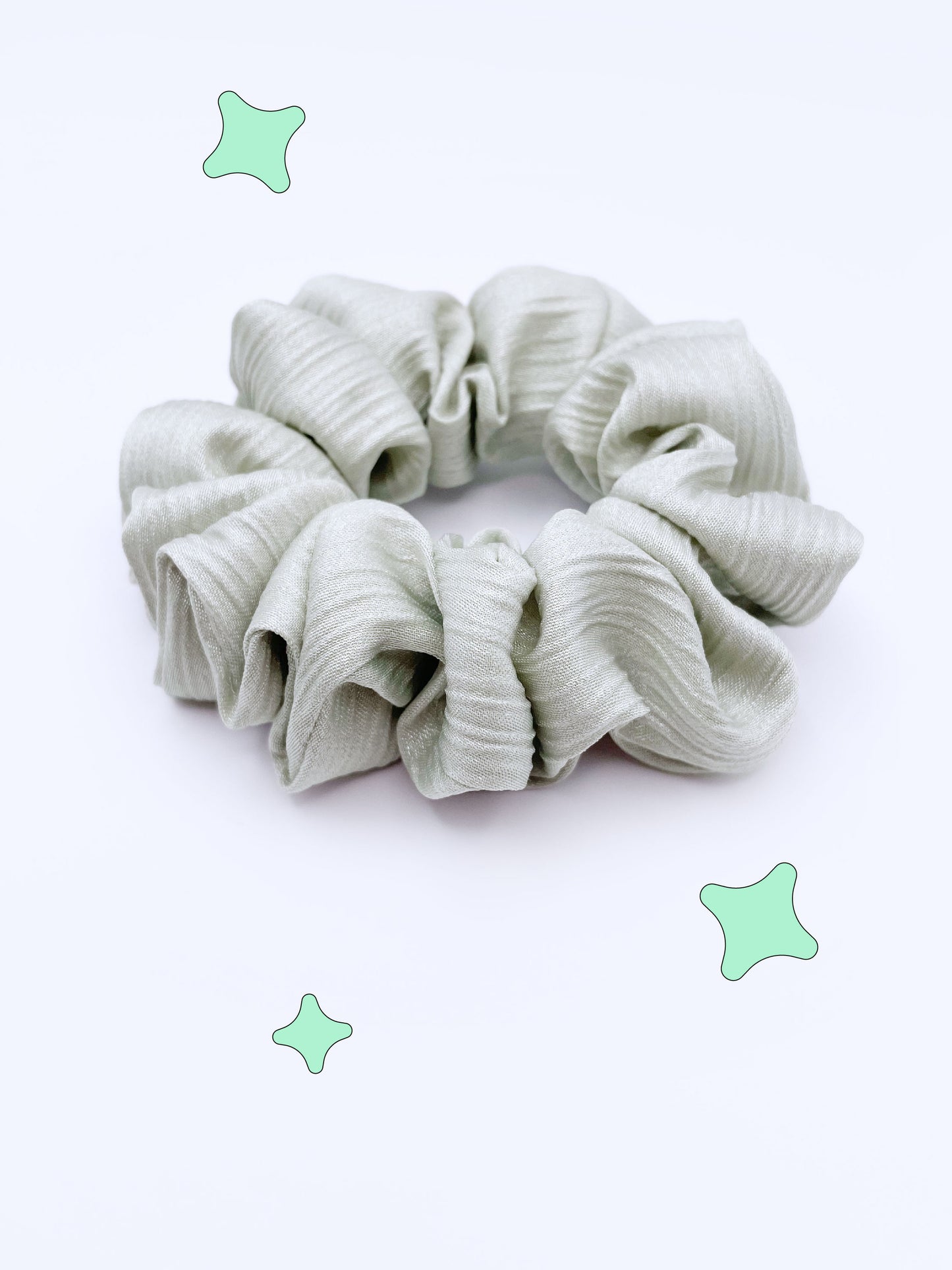 A scrunchie made with a sage green crinkle satin fabric.