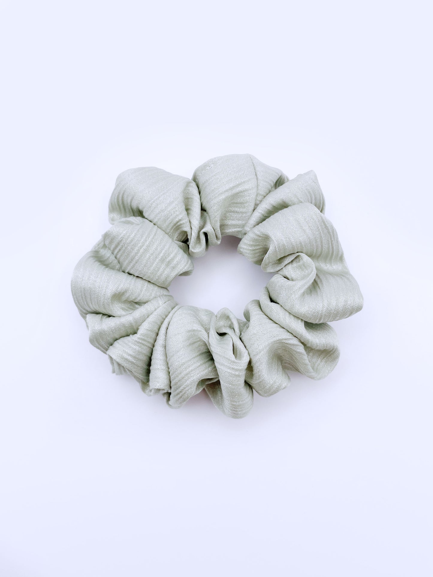 A scrunchie made with a sage green crinkle satin fabric.