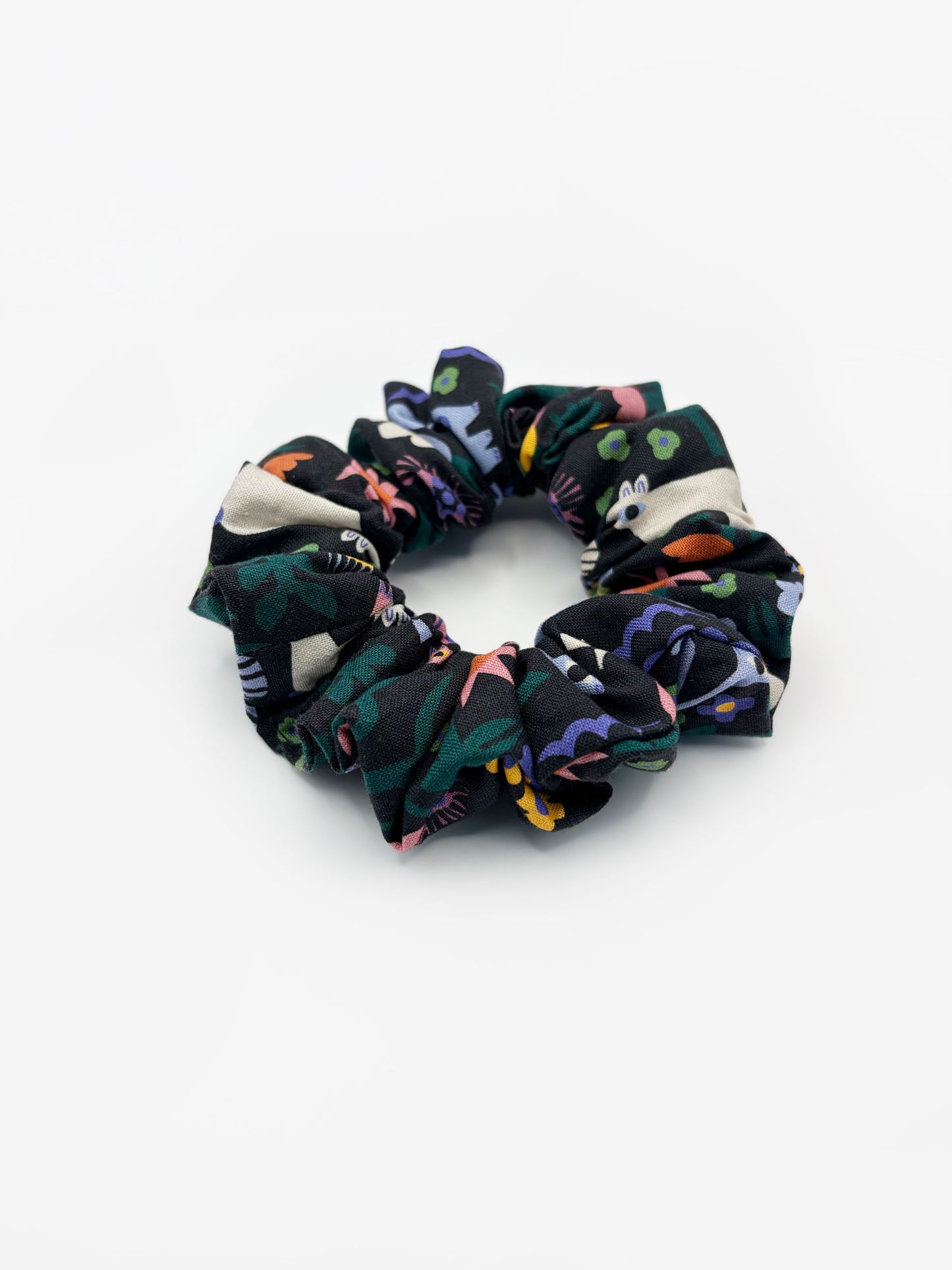 A black scrunchie with a colorful abstract forest print featuring playful florals, leaves, and bright animals.