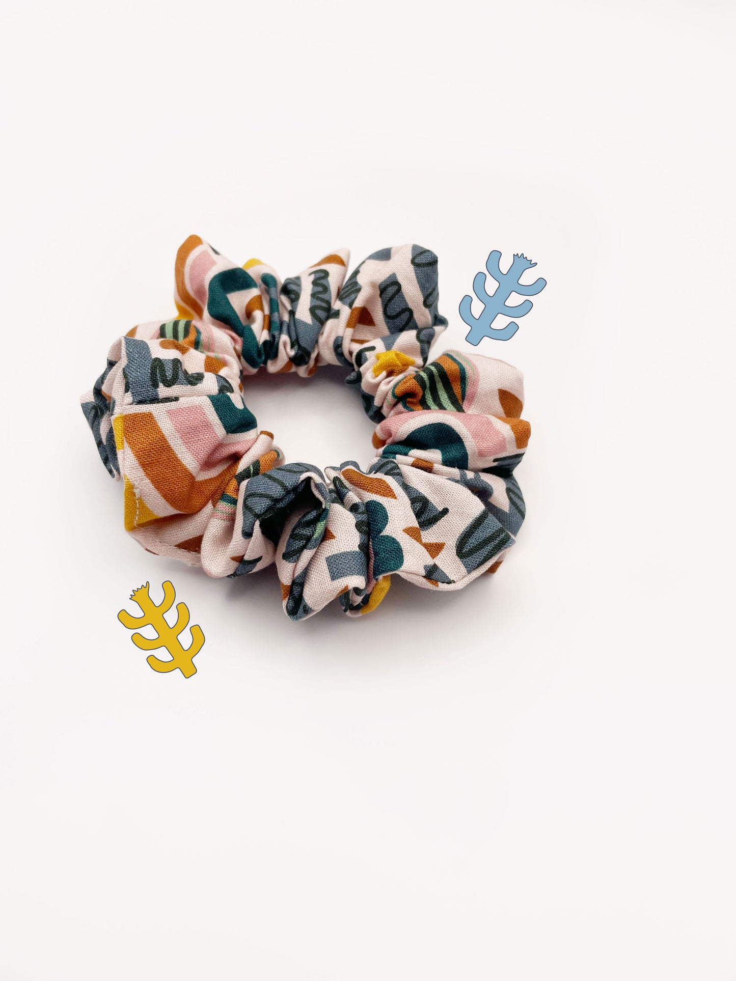 A scrunchie featuring a bold nature-inspired print of bugs, plants, suns, and rainbows.