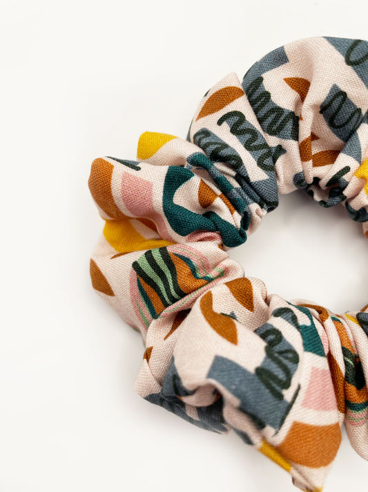 A scrunchie featuring a bold nature-inspired print of bugs, plants, suns, and rainbows.