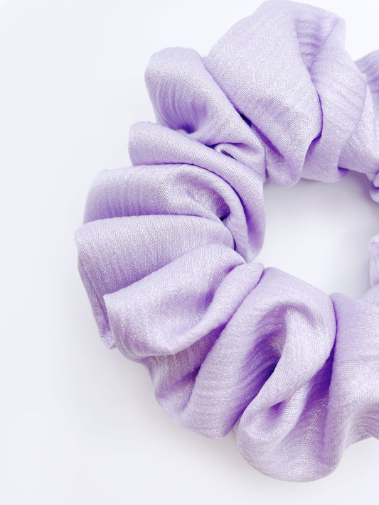 A scrunchie made with a light purple, lavender crinkle satin fabric.