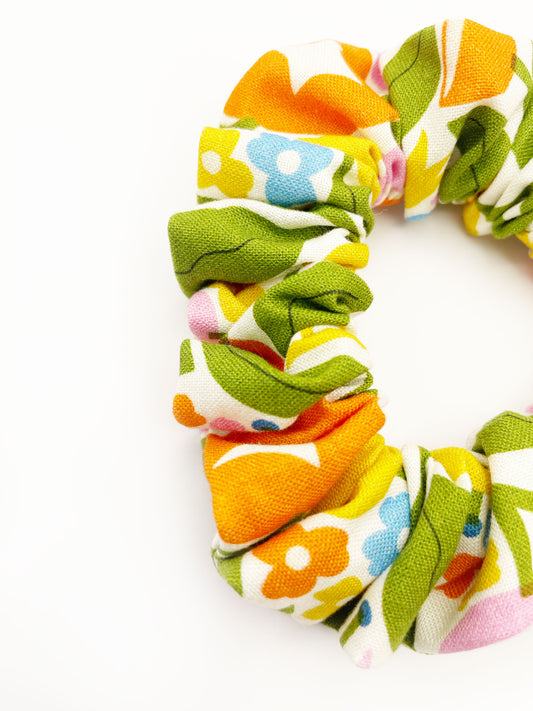A closeup of a vibrant scrunchie with bold yellow, orange, and pink flowers.