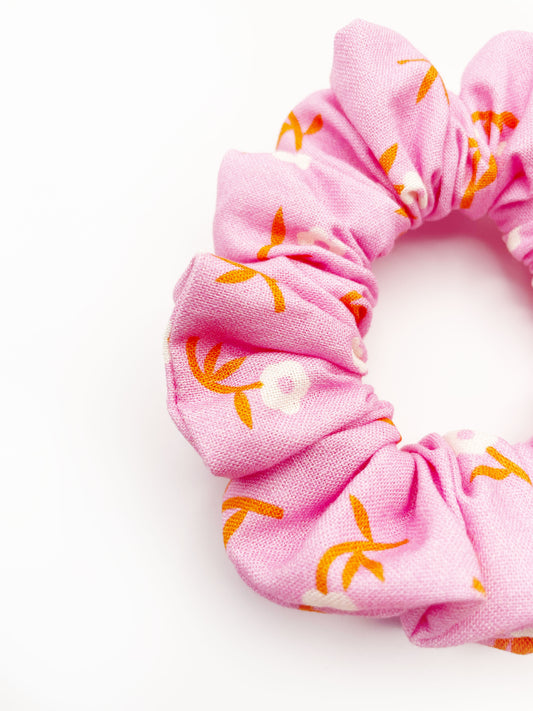 A closeup of a cheerful pink scrunchie with orange-stemmed flowers.