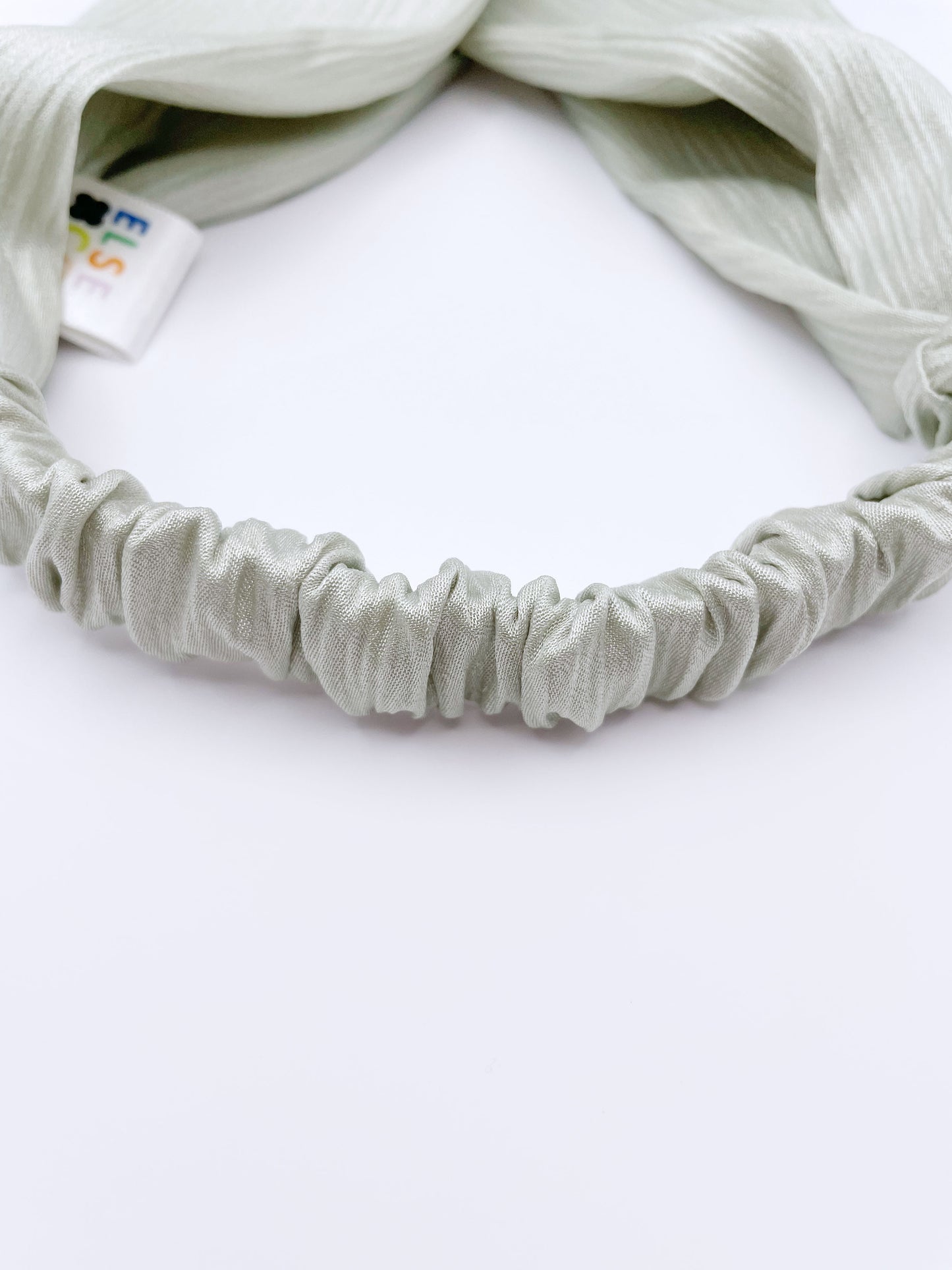 A twist headband made with a pastel green crinkle satin fabric. The headband has an elastic band in the back.