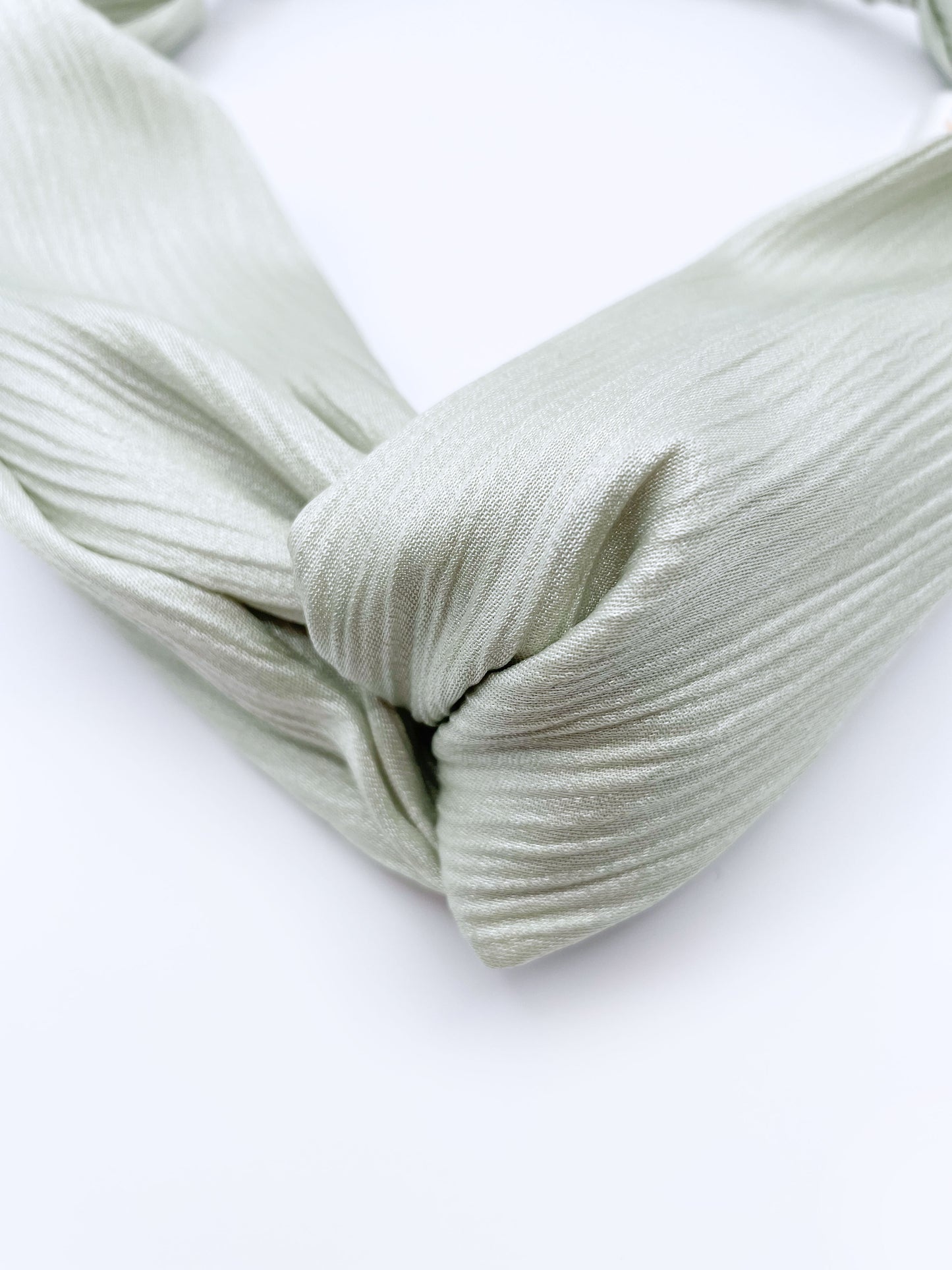 A twist headband made with a pastel green crinkle satin fabric.