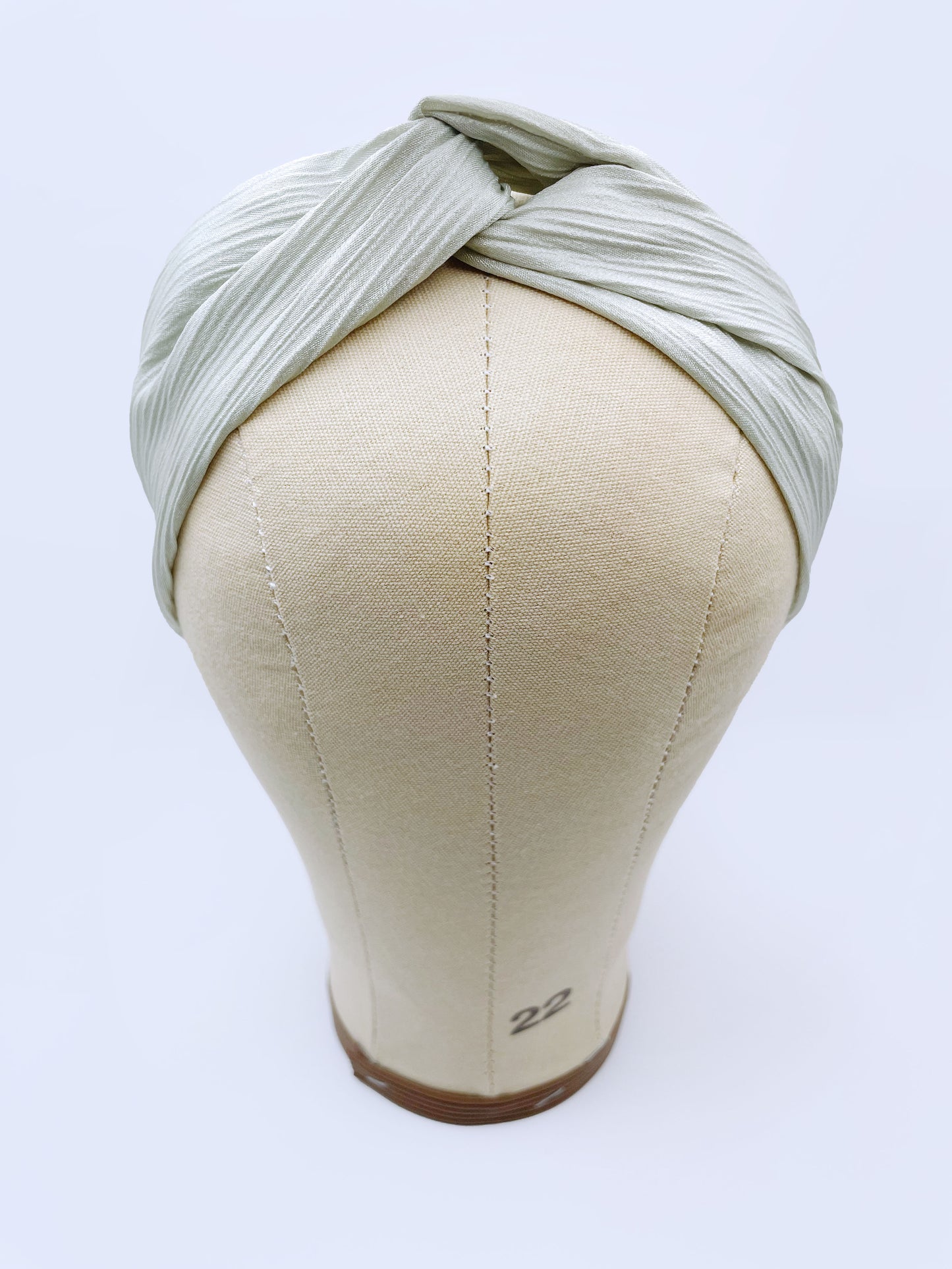 A twist headband made with a pastel green crinkle satin fabric. The headband is on a mannequin head.