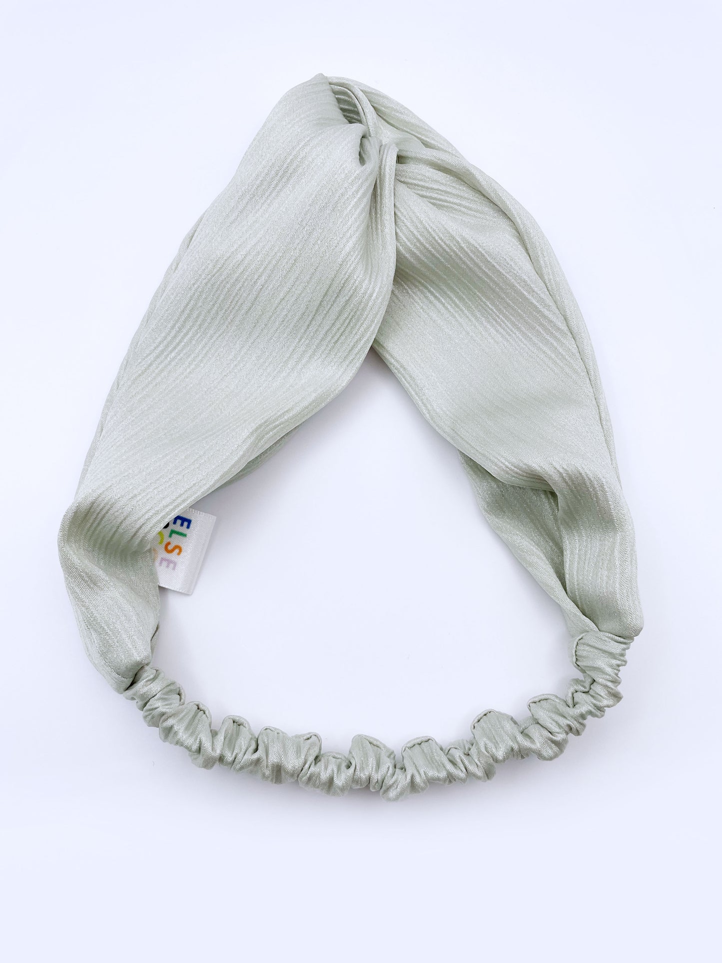 A twist headband made with a pastel green crinkle satin fabric. The headband has an elastic band in the back.