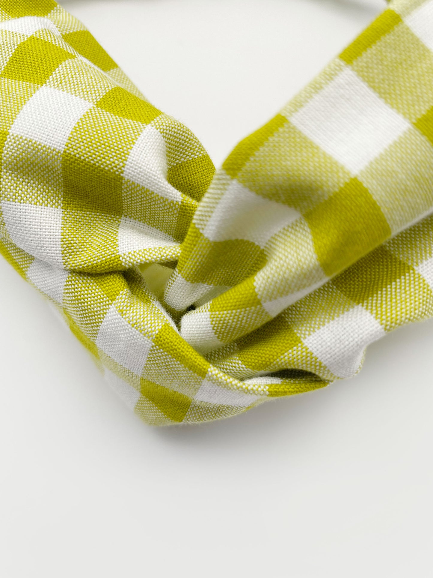 A handmade twist headband with a green and white gingham plaid print. The headband has an elastic band in the back.