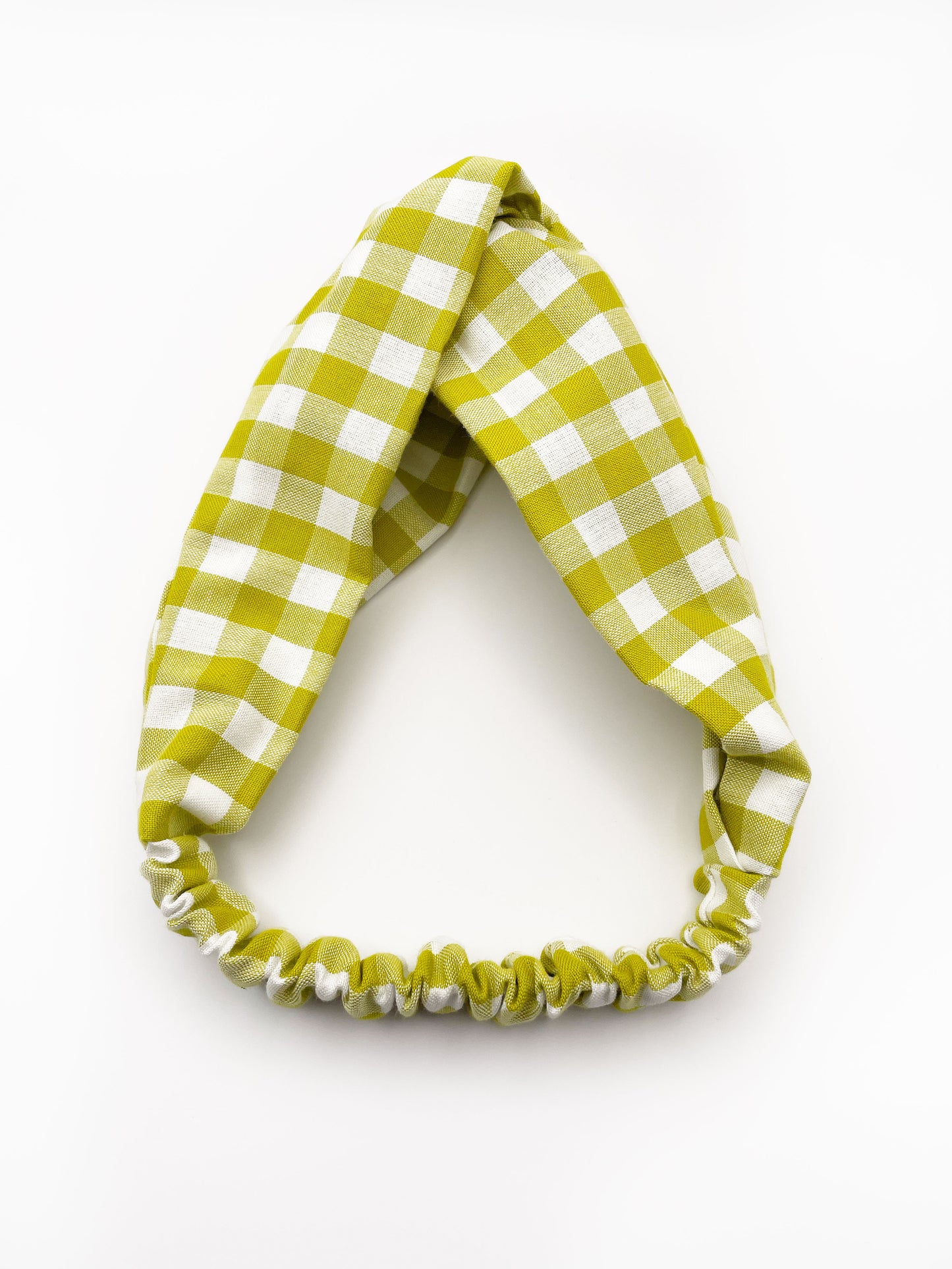 A handmade twist headband with a green and white gingham plaid print. The headband has an elastic band in the back.