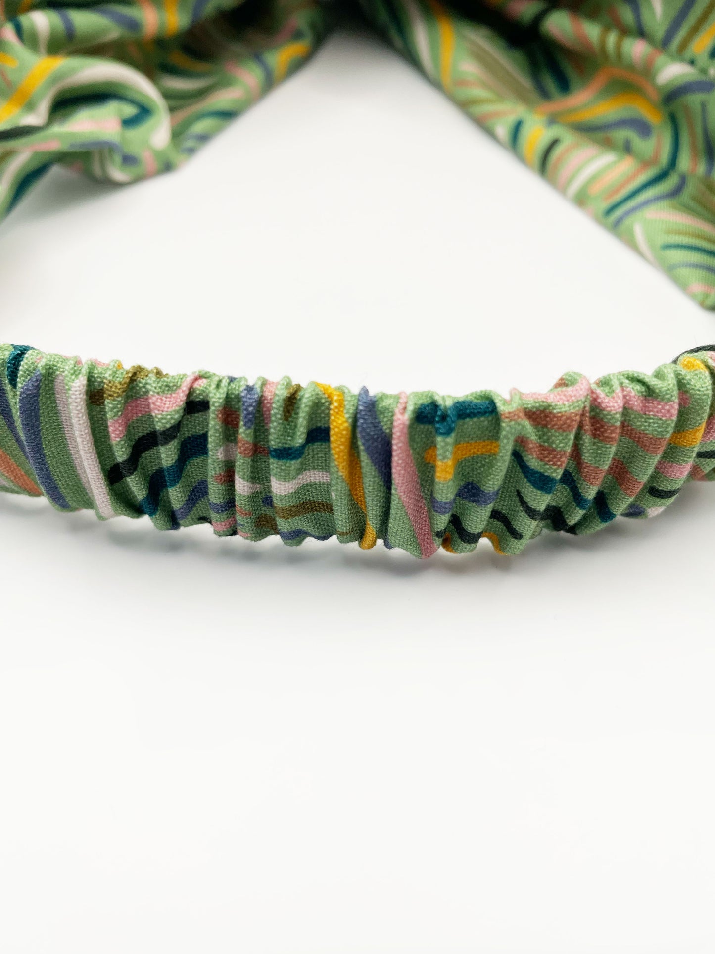 A twist headband made from high-quality cotton with an abstract design inspired by desert rain patterns. The headband has an elastic band in the back.