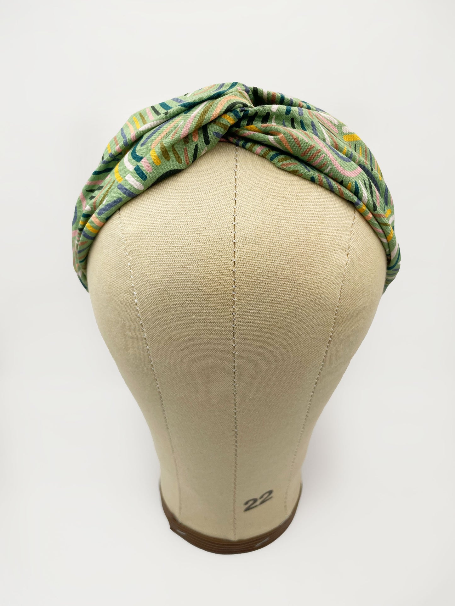 A twist headband made from high-quality cotton with an abstract design inspired by desert rain patterns. The headband is shown on a mannequin head.