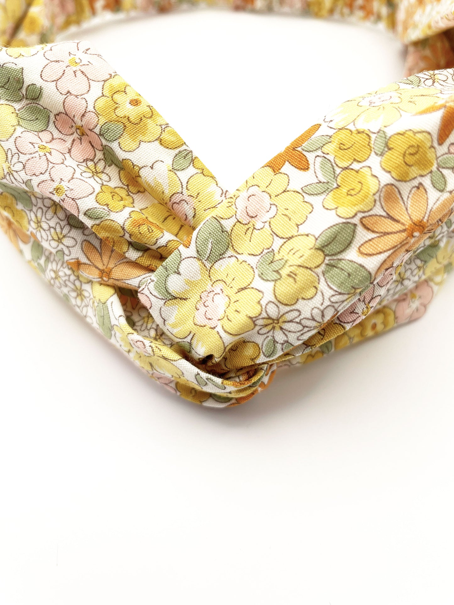 A handmade yellow floral twist headband with an elastic band in the back.