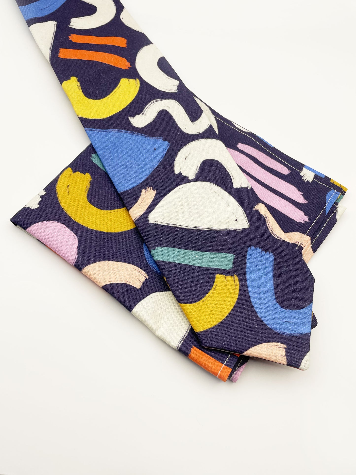 A cotton necktie with a colorful abstract print featuring various doodles shown with a matching pocket square.