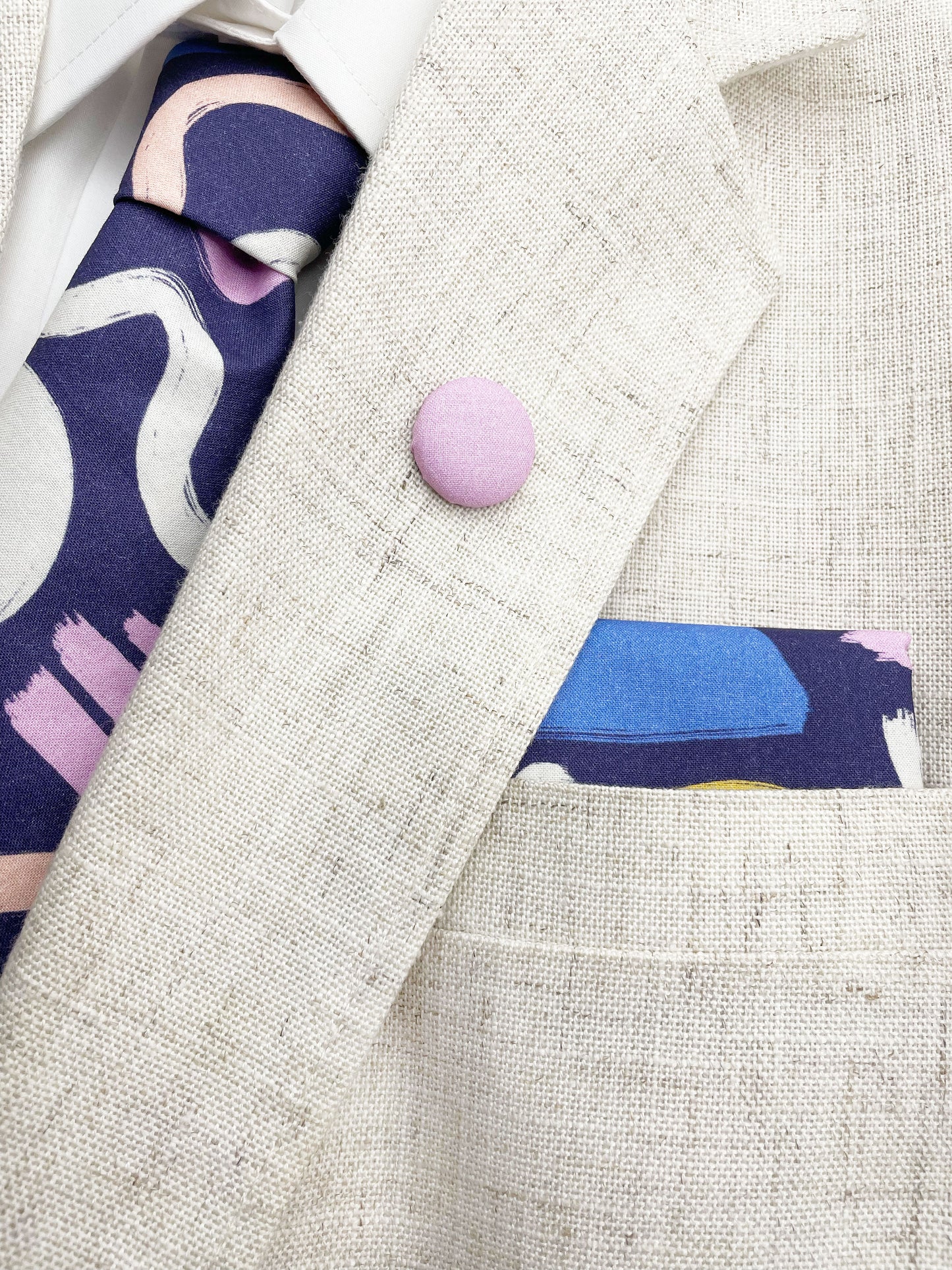 A cotton necktie with a colorful abstract print featuring various doodles shown with a matching pocket square and lapel pin.
