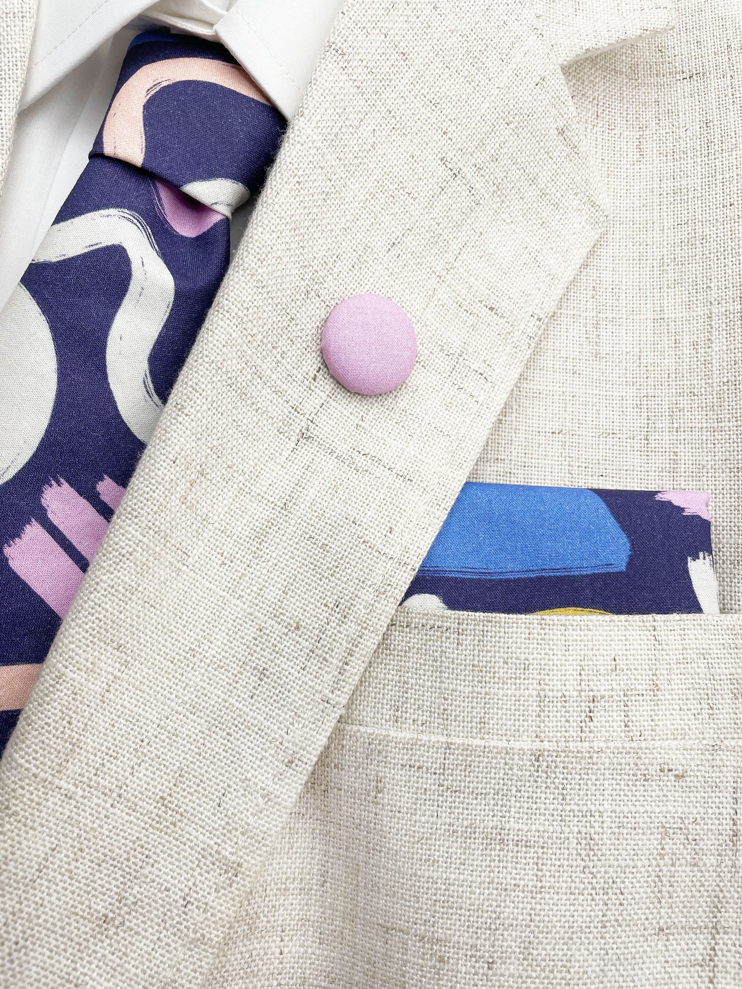 A cotton handmade pocket square with a colorful abstract print featuring various doodles shown with matching necktie and lapel pin.
