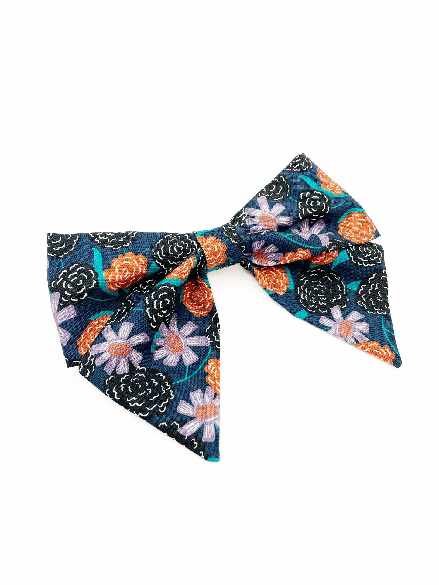 A large handmade hair bow with vivid orange, lavender, and black flowers, accented with fresh green leaves. The cotton fabric is attached to a sturdy barrette clip.
