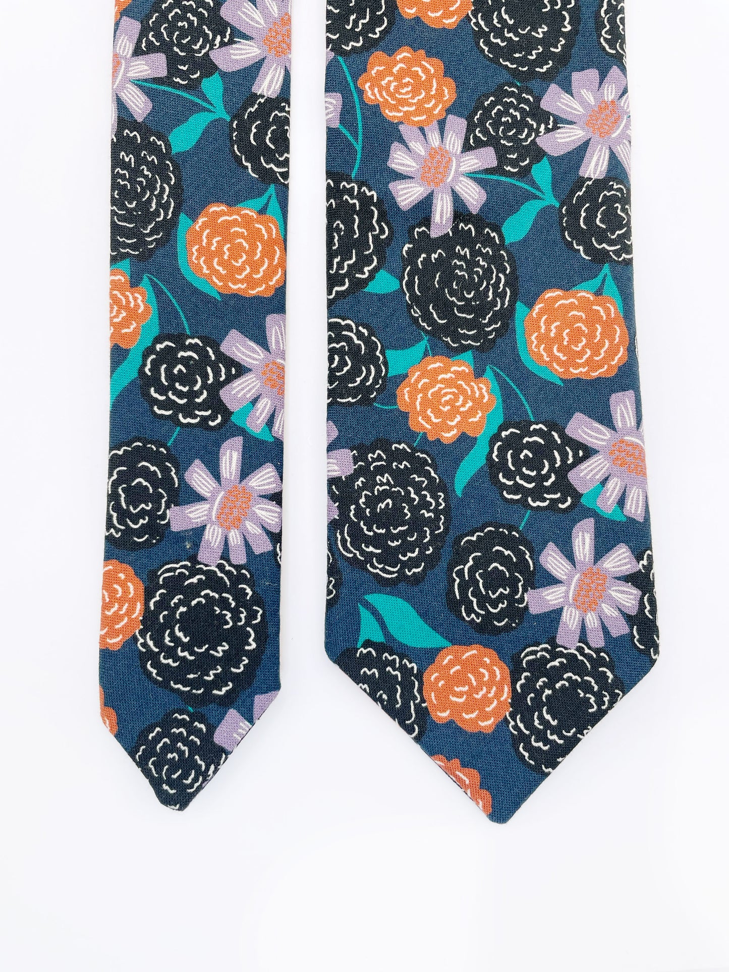 A navy blue necktie with vivid orange, lavender, and black flowers, accented with fresh green leaves.