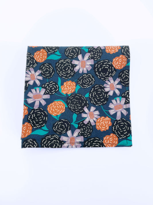 A navy blue pocket square with vivid orange, lavender, and black flowers, accented with fresh green leaves.
